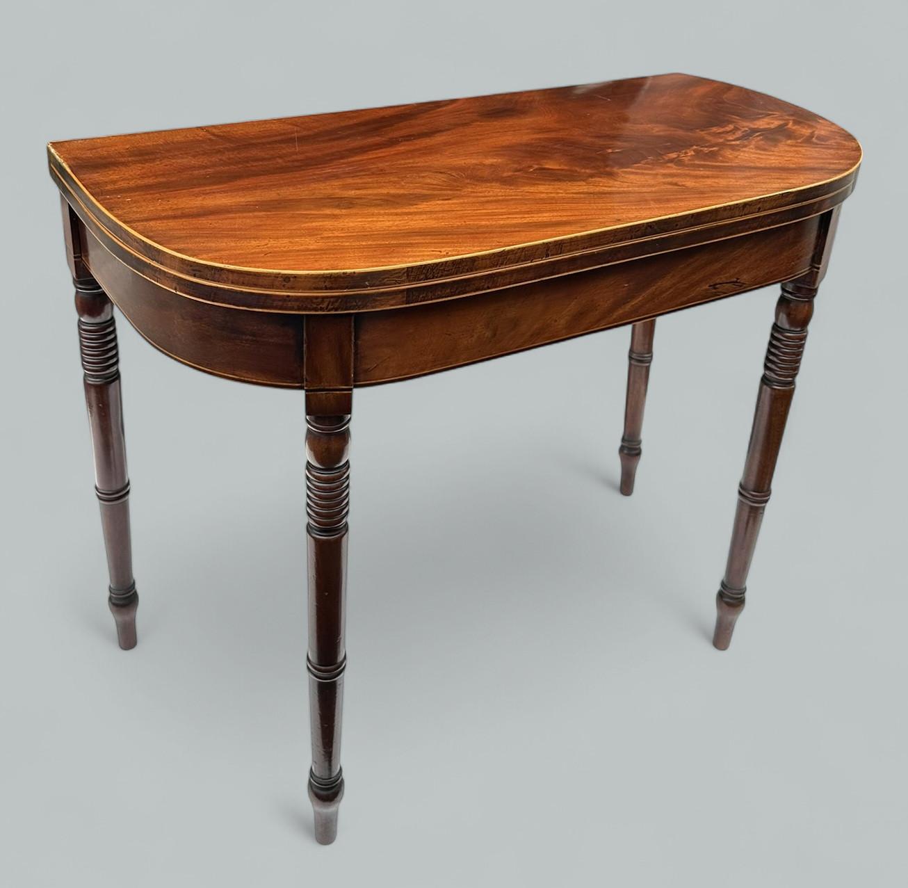 Elegante mesa de juego inglesa georgiana de caoba flameada de extraordinaria calidad, principios del siglo XIX. Alrededor de 1820.  

El tablero plegable de forma rectangular con esquinas frontales redondeadas, elevado sobre patas torneadas, el