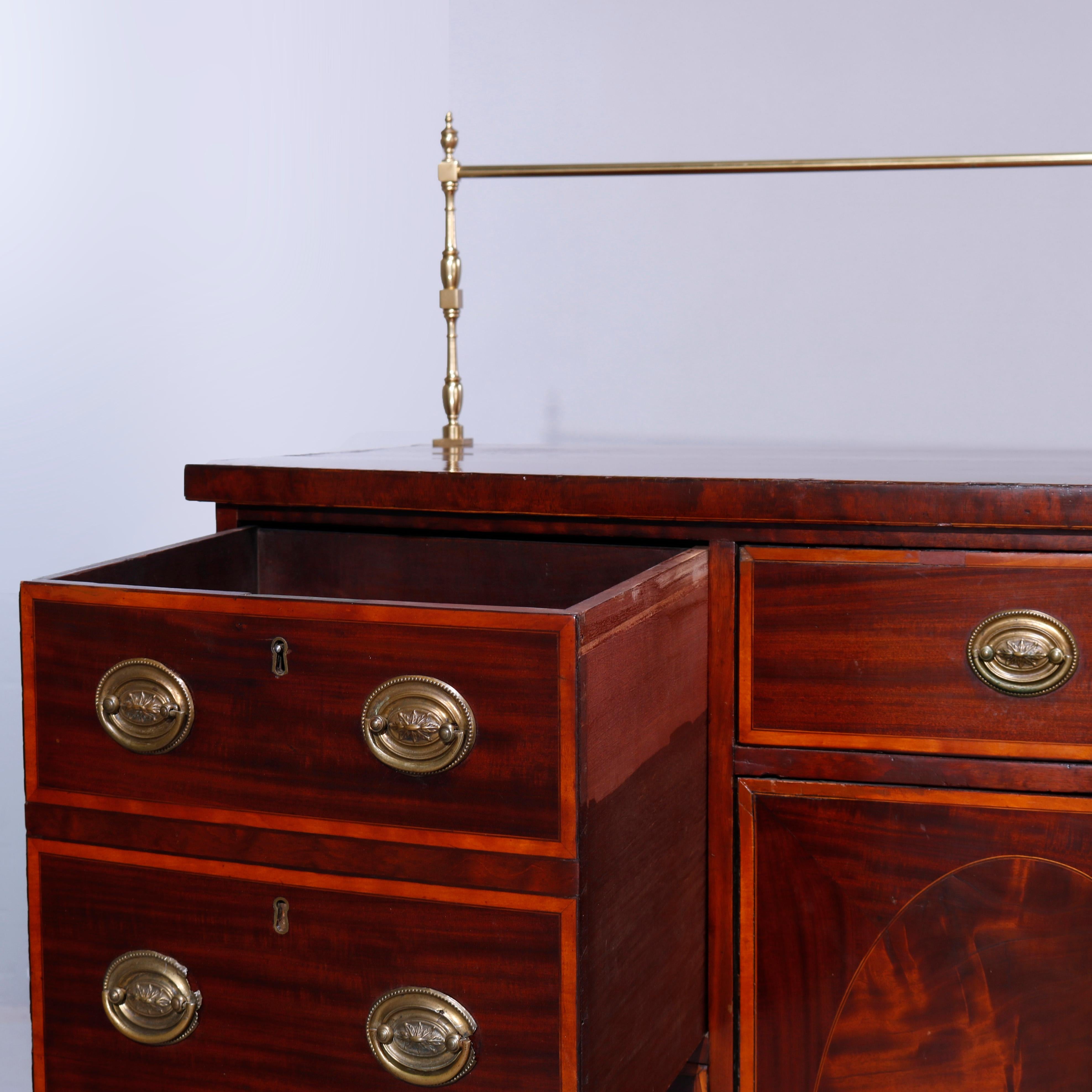 An antique English Georgian sideboard offers flame mahogany construction with brass plate rail and bow front having drawers and cabinets with inlaid reserves and satinwood banding, raised on bracket feet, c1810

Measures - 55''H x 65.75''W x