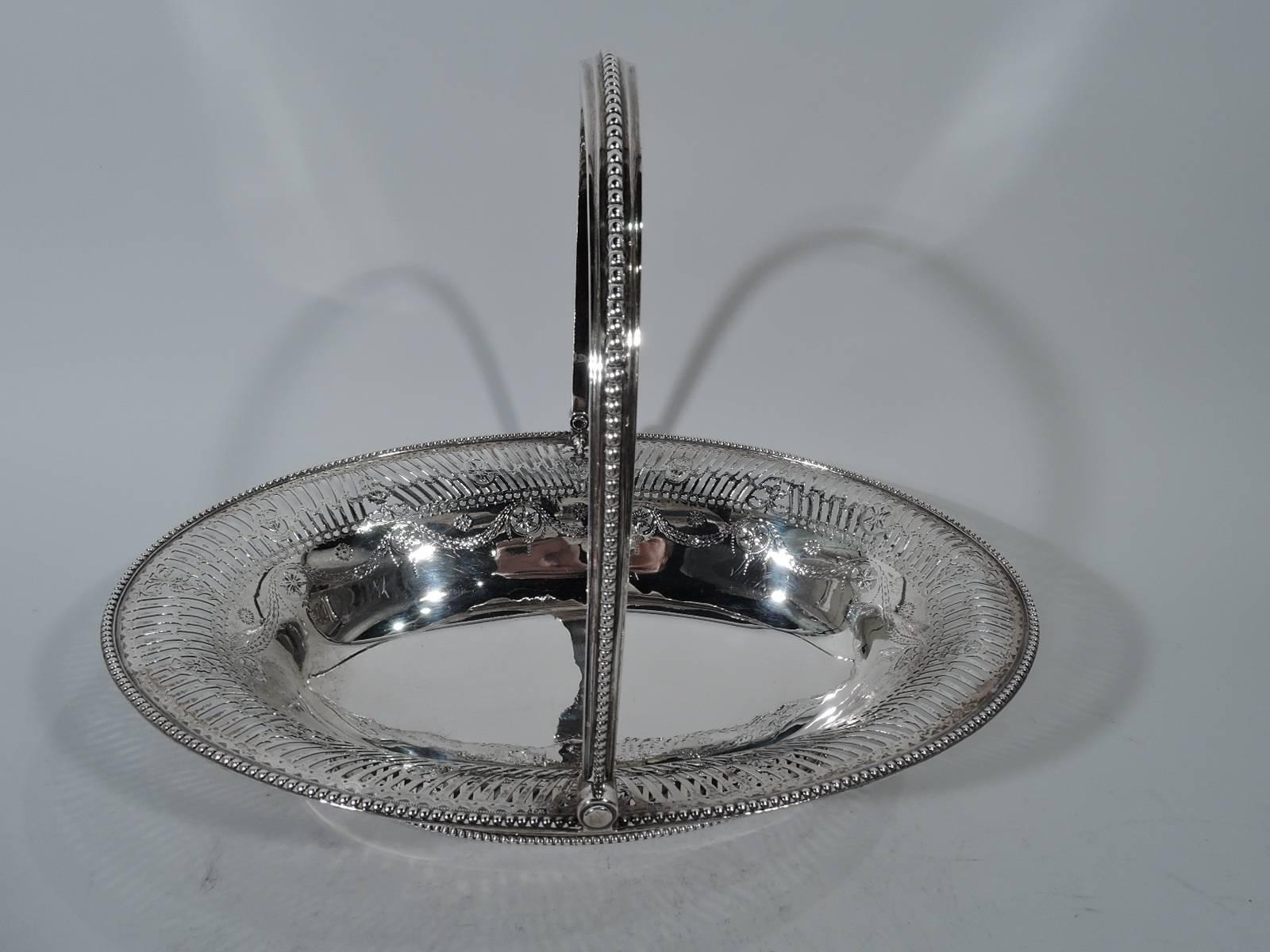 George III sterling silver basket. Made by William Plummer in London in 1782. Oval bowl with swing c-scroll handle and oval foot. Beaded rims and handle, and pierced lines and oval frames inset with vases and flowers. Interior has engraved garland.