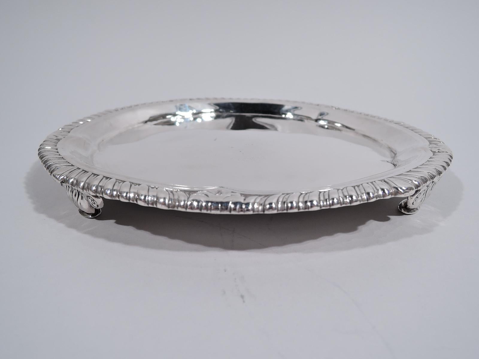 George IV sterling silver salver. Made by John Bridge of Rundell, Bridge & Rundell in London in London in 1824. Round with well and shallow lobing. Rim gadrooned with interspersed leaves. Four volute capital supports. Fully marked. Weight: 12 troy