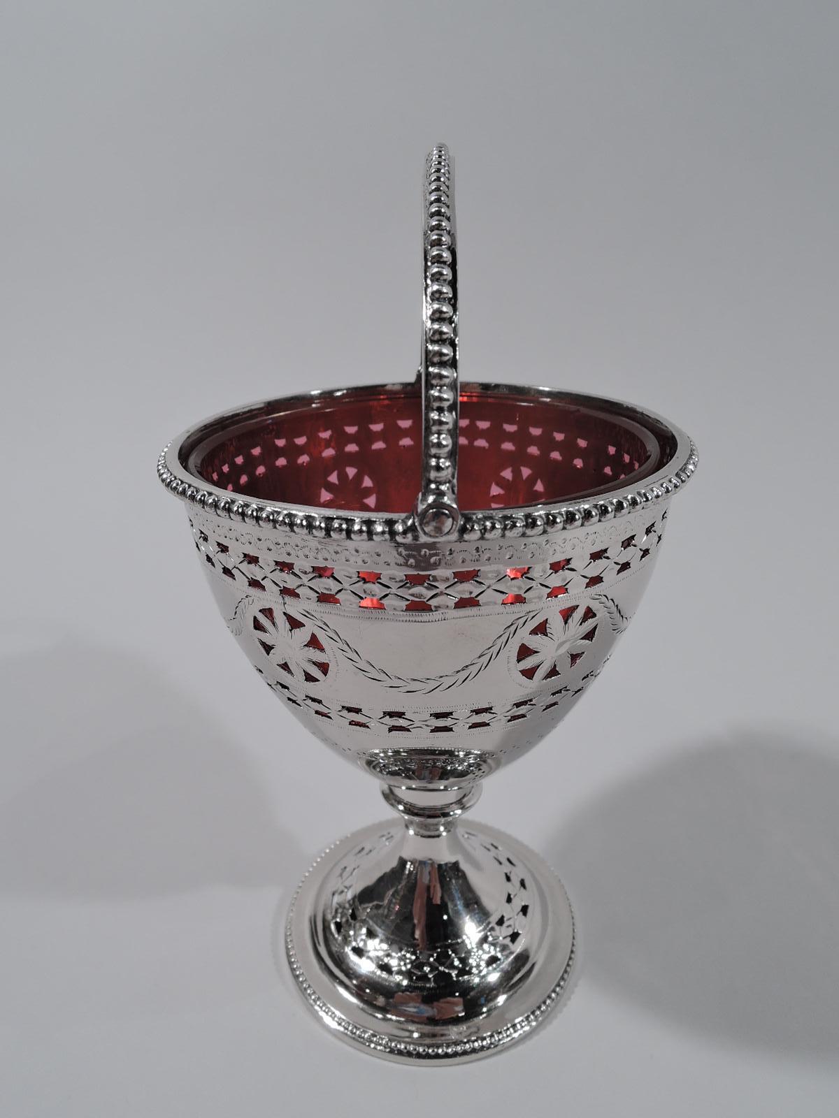 English Georgian Neoclassical sterling silver sugar basket, 1783. Conical bowl on knopped stem flowing into raised foot. Rims beaded; C-scroll swing handle same. Pierced flower head borders and paterae joined by engraved swag. Detachable red glass
