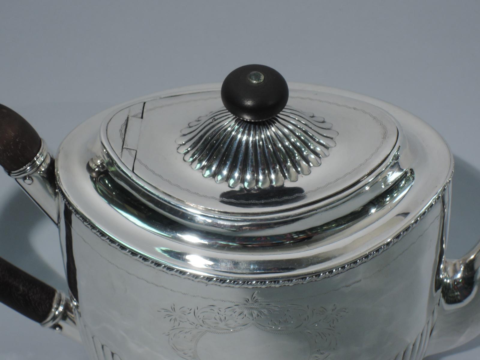 George III sterling silver teapot. Made by George Eadon & Co. in Sheffield in 1800. Ovoid with half fluting. Capped scroll handle in stained wood. S-scroll spout. Hinged cover with lobed dome and round stained-wood finial. Engraved heraldic
