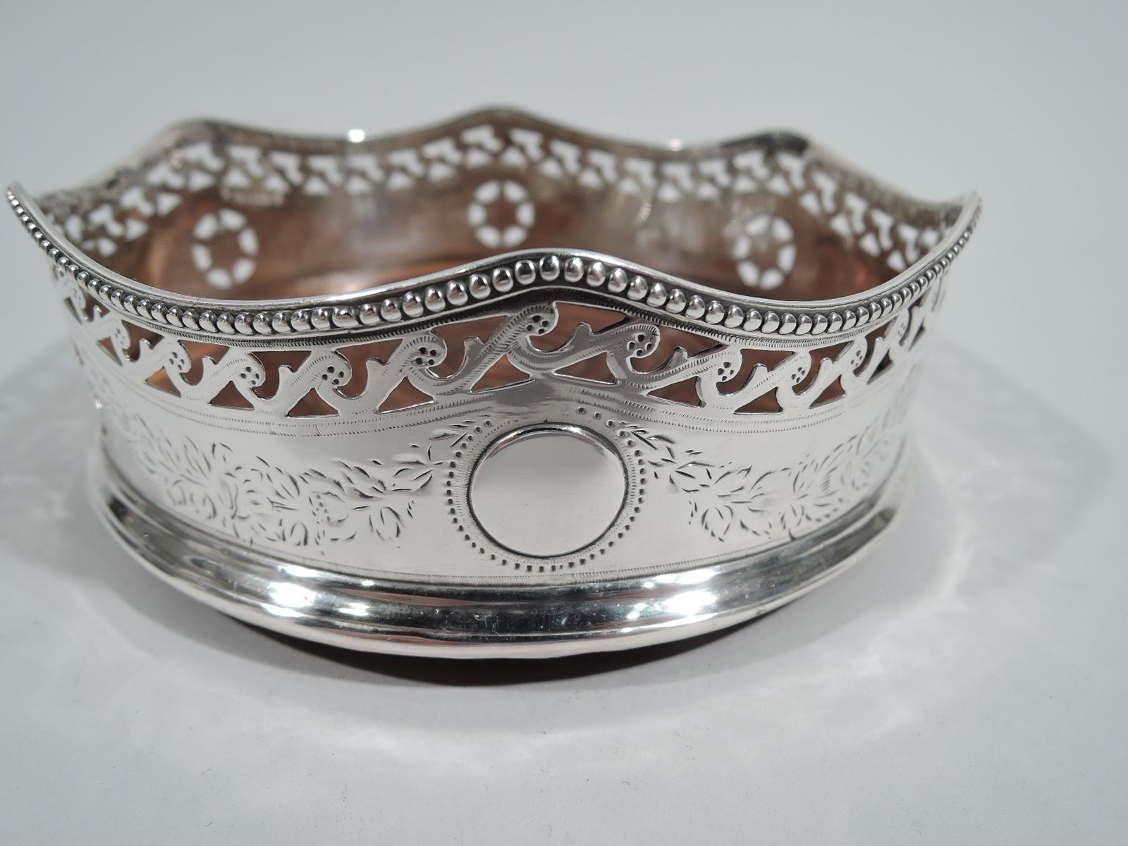 English Georgian sterling silver wine coaster, 1814. Engraved garland alternating with pierced paterae; single solid round frame (vacant). Wavy beaded rim and pierced Vitruvian scroll border. Stained-wood base and felt-lined underside. A