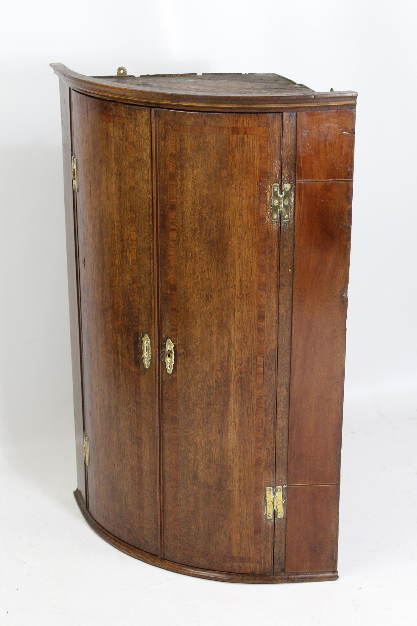 An attractive antique George III oak corner cupboard with barrel front with mahogany, satinwood and ebony banding dating from the late 18th century. It has attractive brass escutcheons and H hinges and comes with lock and working key. The twin doors