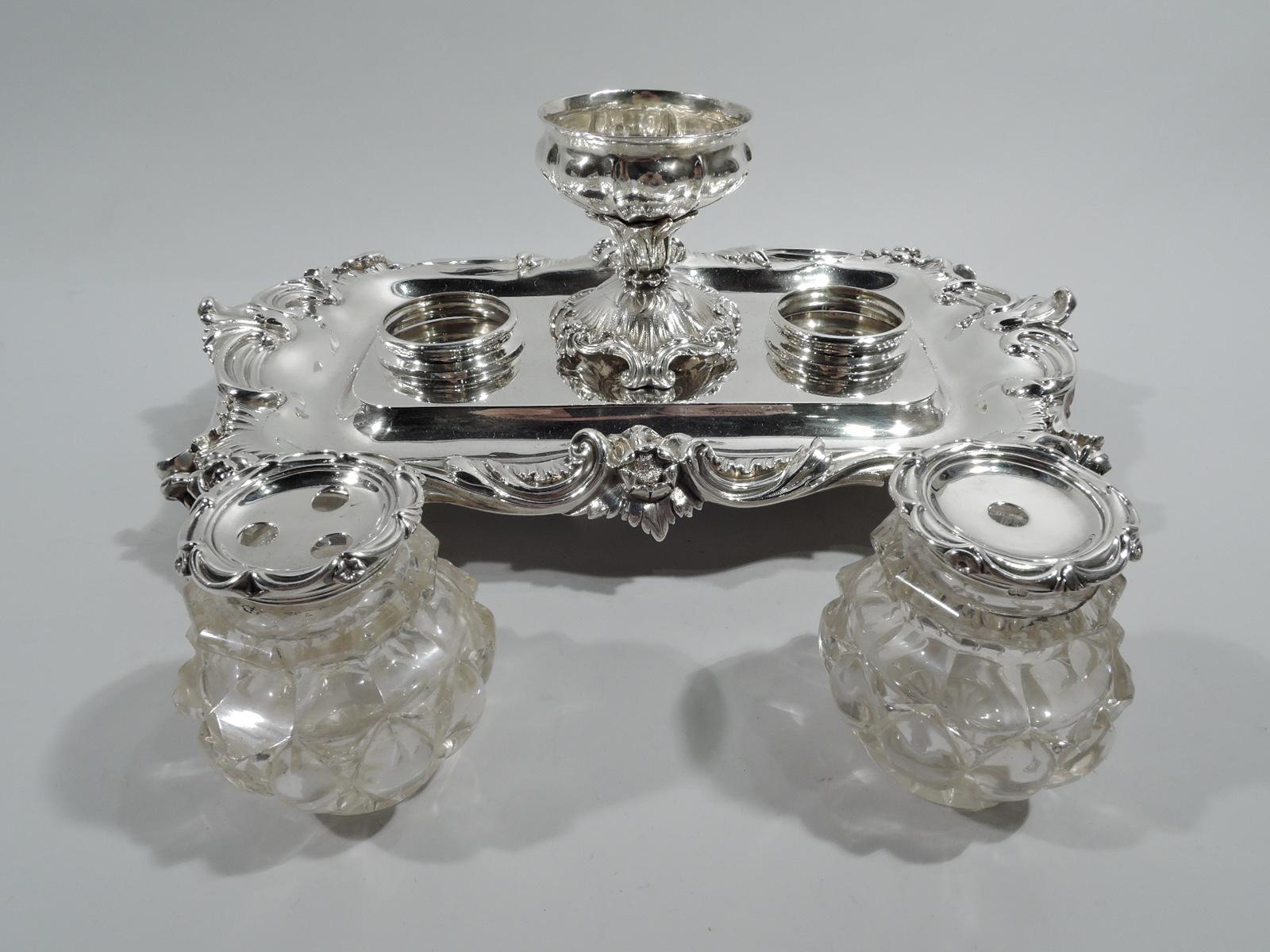 George IV sterling silver inkstand. Made by Barnard & Sons, Ltd in London in 1832. Stand has plain rectilinear well with curved corners and mounted wafer bowl set in leafy mount on spread and scrolled foot between rings supporting inkpot and sander.