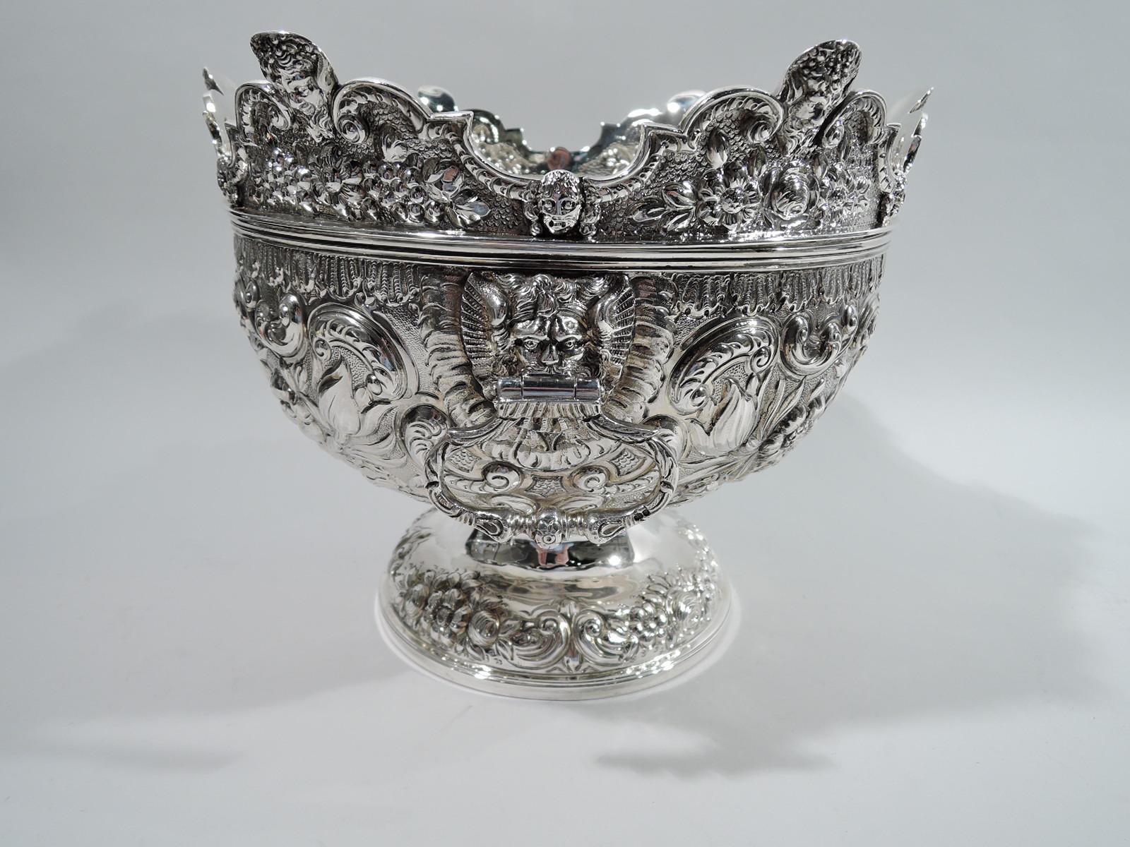 George IV sterling silver monteith. Made by Samuel Whitford in London in 1823. Round and curved bowl; at sides male heads in leonine surrounds with loose-mounted rings. Chased and repousse flowers and scrolls, and two scrolled cartouches engraved