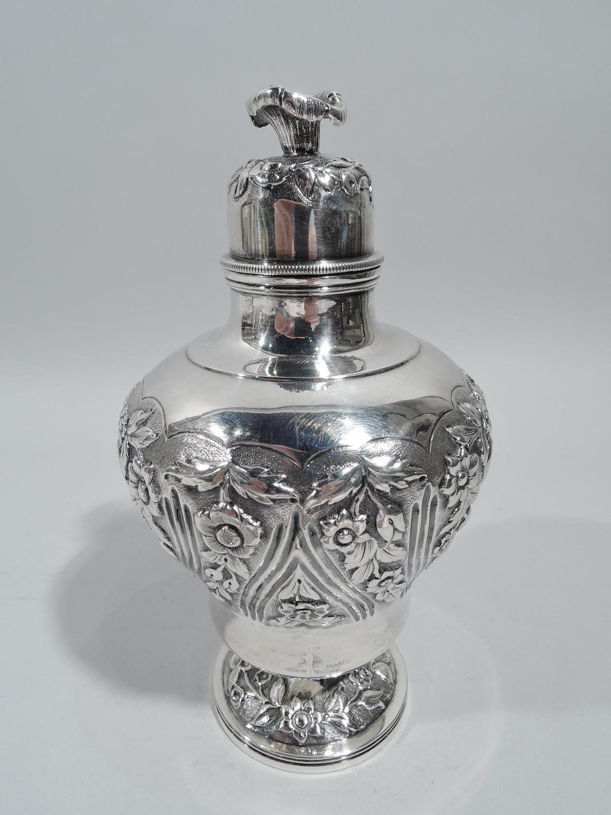 George IV sterling silver tea caddy. Made by Richard Pierce & George Burrows in London in 1829. Baluster with raised foot. Short neck and domed cover with flower finial. Chased floral garlands on stippled ground. On body garlands alternate with