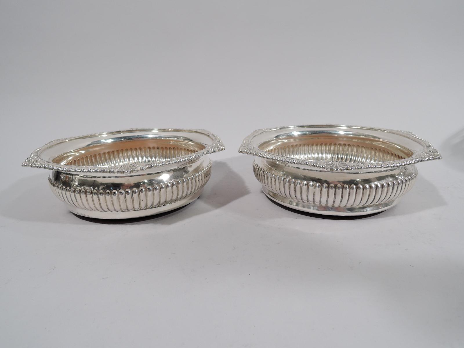 Pair of George III sterling silver wine bottle coasters, 1818. Each: Bellied with horizontal ribbing. Everted egg-and-dart rim interspersed with leaves and shells. Interior stained wood; central sterling silver medallion has engraved armorial.