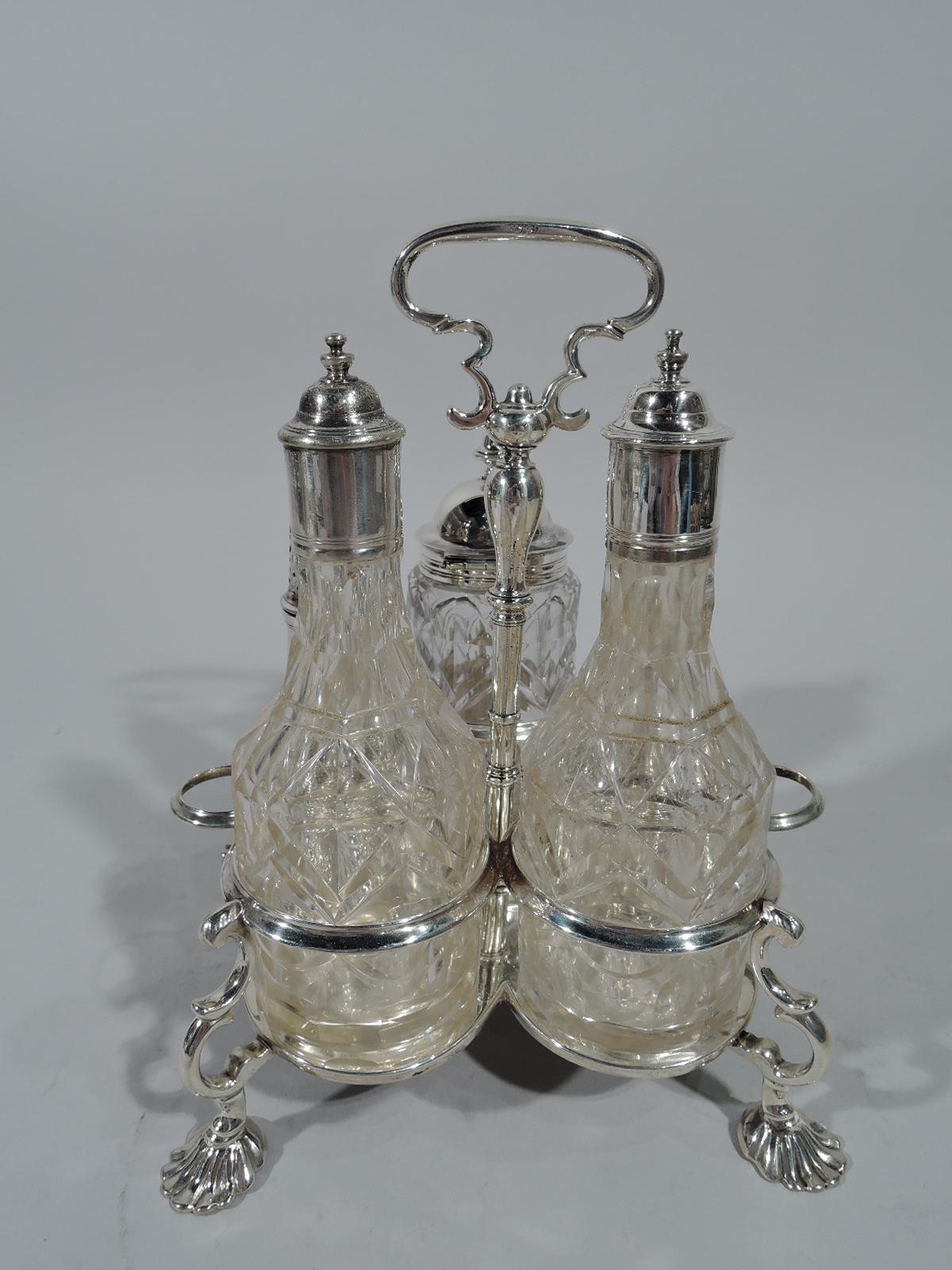 George II sterling silver cruet stand. Made by Samuel Wood in London in 1752. Cinquefoil base with four double-scroll mounts supporting seven-ring frame (of which two for stoppers). Each mount terminates in scallop shell foot. Central knopped pole