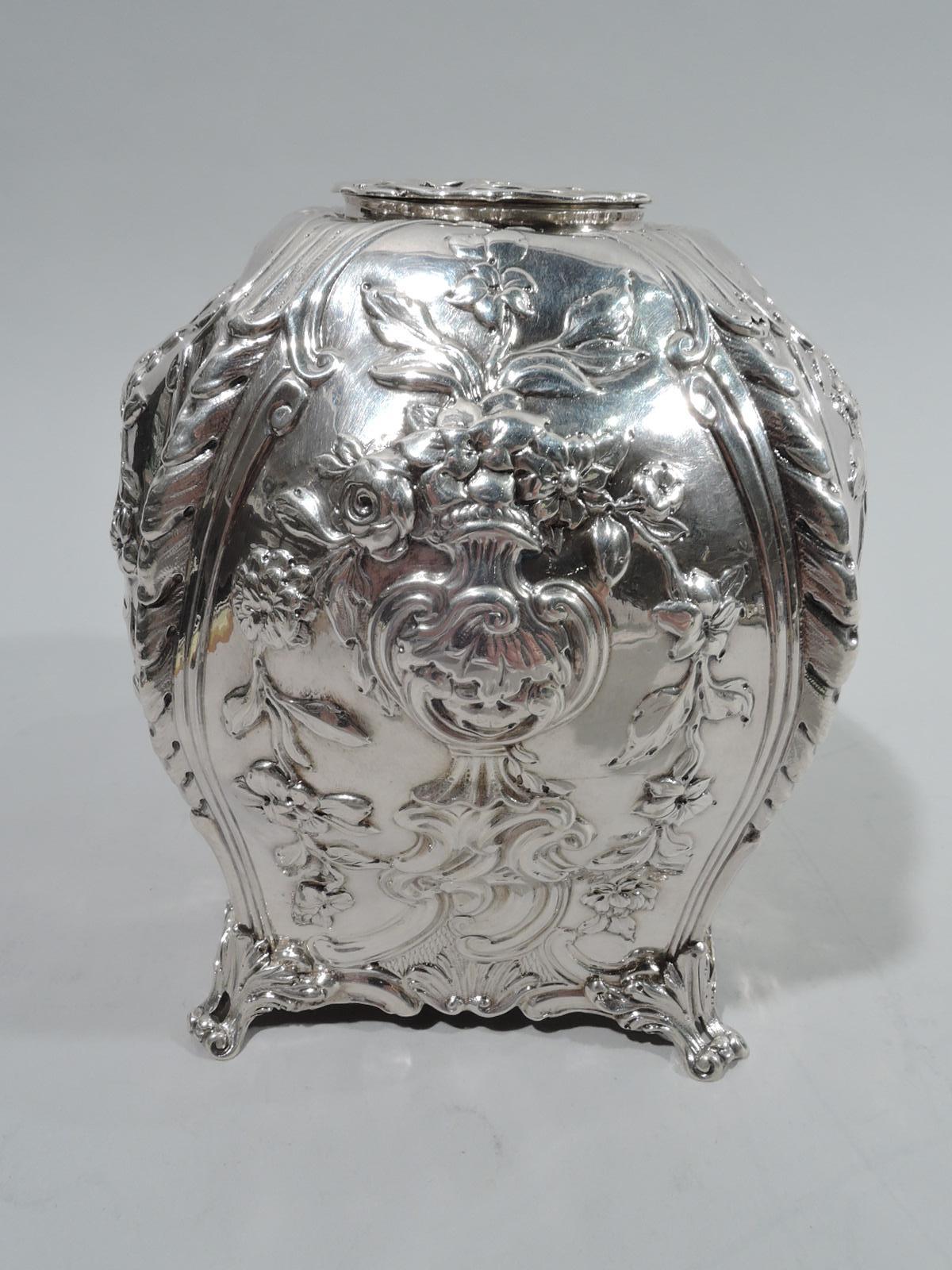English Georgian Rococo sterling silver tea caddy, 1766. Bombe with corner leaf-mounted volute scroll supports. Chased scrollwork and flower baskets framed by garlands. Asymmetrical cartouche engraved with armorial bird. Round and flat cover central