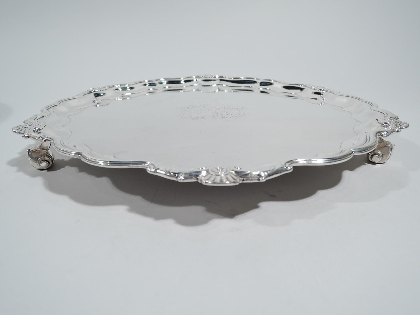George II sterling silver salver. Made by George Wickes in London in 1747. Molded and scrolled piecrust rim interspersed with scallop shells. Well center has engraved armorial with raised spear. Three capped volute supports. Fully marked. Weight: 26