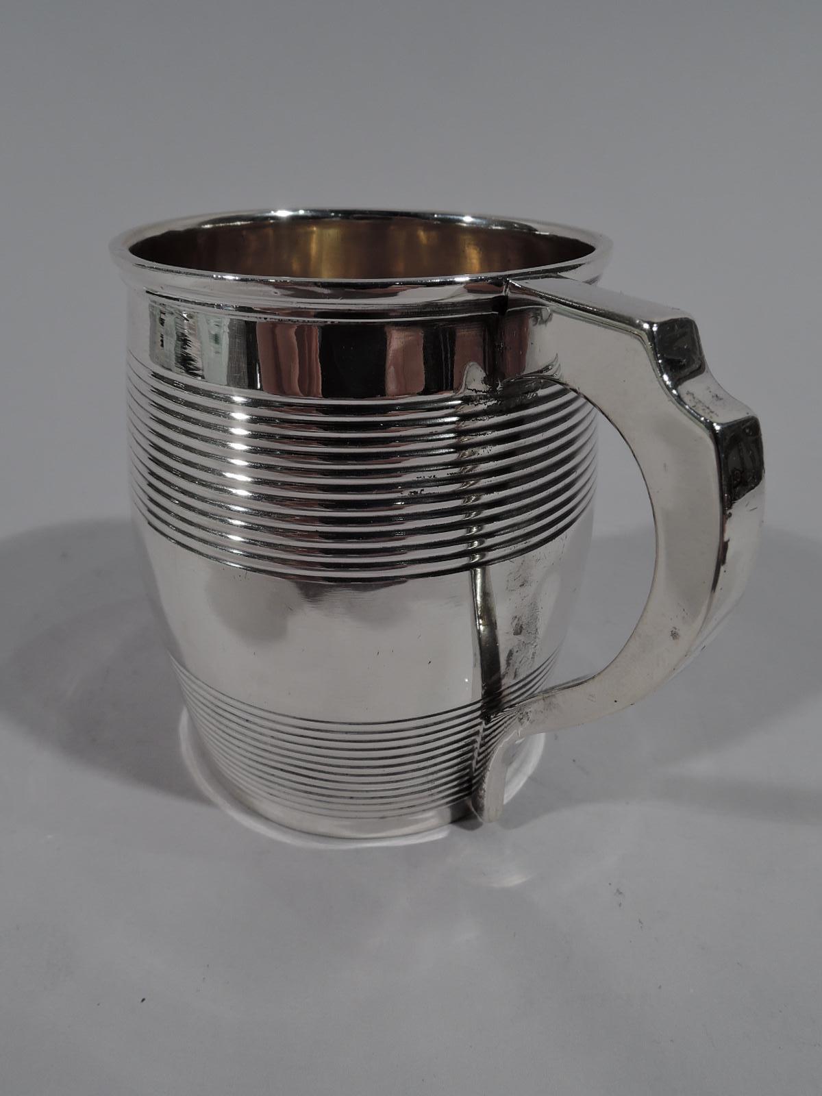 George III sterling silver christening mug. Made by Elizabeth Morley in London in 1809. Barrel form with scroll bracket handle. Reeded “hoops” at top and bottom. Middle vacant. Fully marked. Weight: 2.5 troy ounces.
