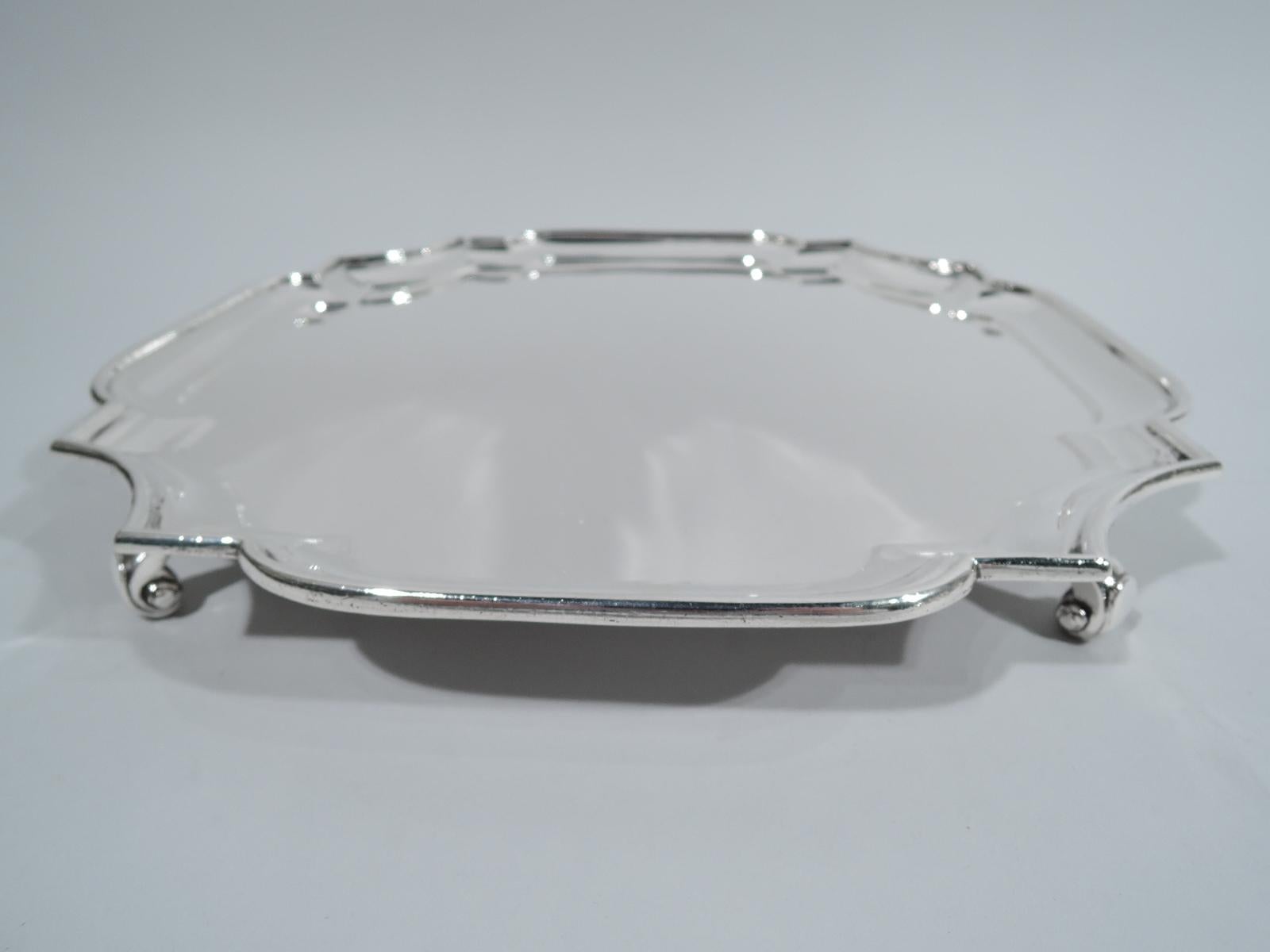 George V sterling silver salver. Made by Goldsmiths & Silversmiths Co. Ltd in London in 1922. Cartouche with 4 curved sides and curvilinear concave corners. Rim molded. Four capped volute supports. Fully marked. Weight: 31.5 troy ounces.