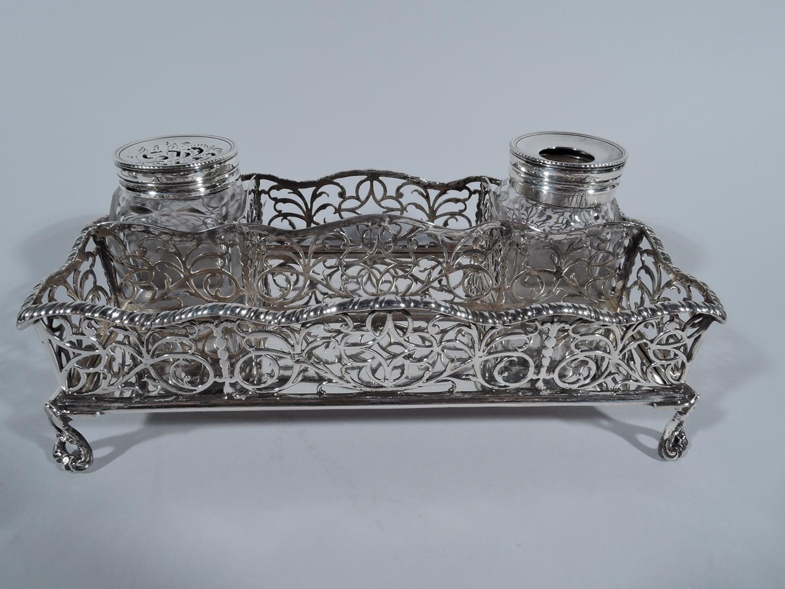 George III sterling silver inkstand. Made by William Plummer in London in 1768. Rectangular with wavy and ornamental open partitions mounted to solid rectangle supported by open corner scroll supports. With ink and sand bottles. An archaic gesture