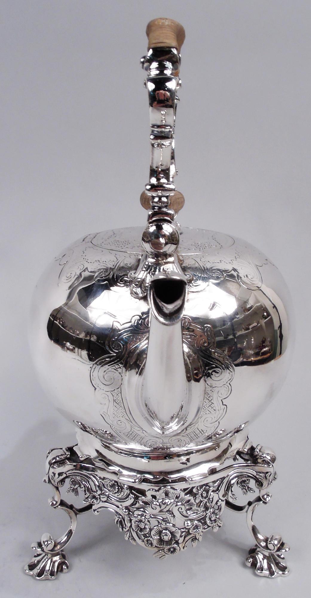 English Georgian sterling silver hot water kettle, 18th century. Globular with s-scroll spout and rattan-wrapped swing handle with scroll supports and mounts. Hinged and flush cover with stained-wood finial. Chased scrollwork, diaper, and scallop