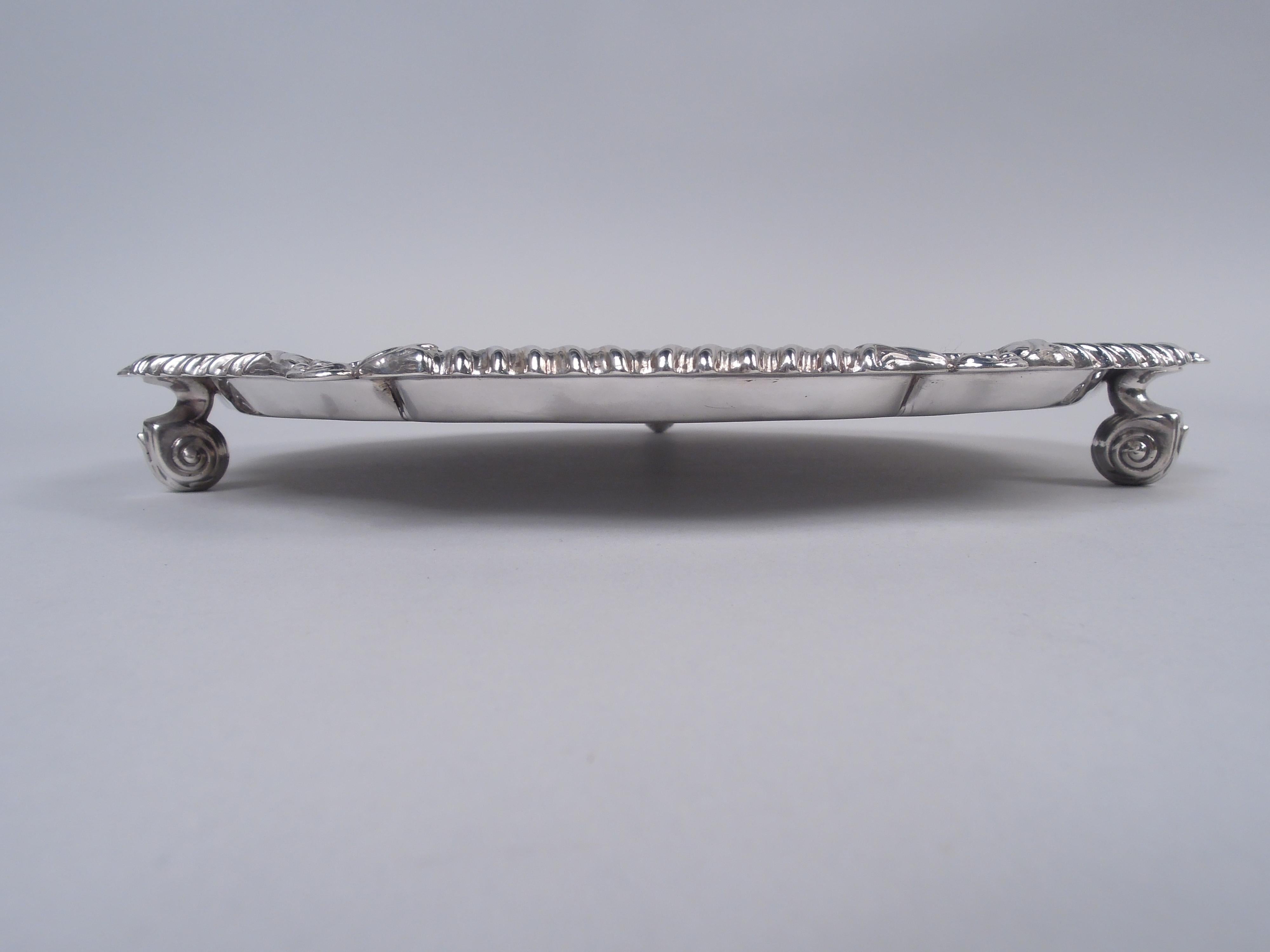 George V sterling silver salver. Made by Lee & Wigfull in Sheffield in 1921. Round and serpentine; rim gadrooned and interspersed with scallop shells. Three leaf-capped volute scroll supports. Fully marked. Weight: 17.5 troy ounces. 