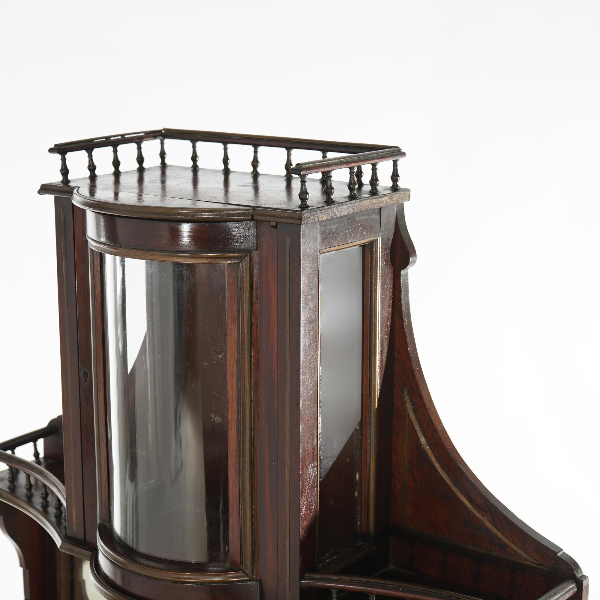 An antique English Georgian curio offers mahogany construction with upper tower having bronze gallery over enclosed display with single curved glass door surmounting lower enclosed display with pull out tray and bronze gallery, raised on straight
