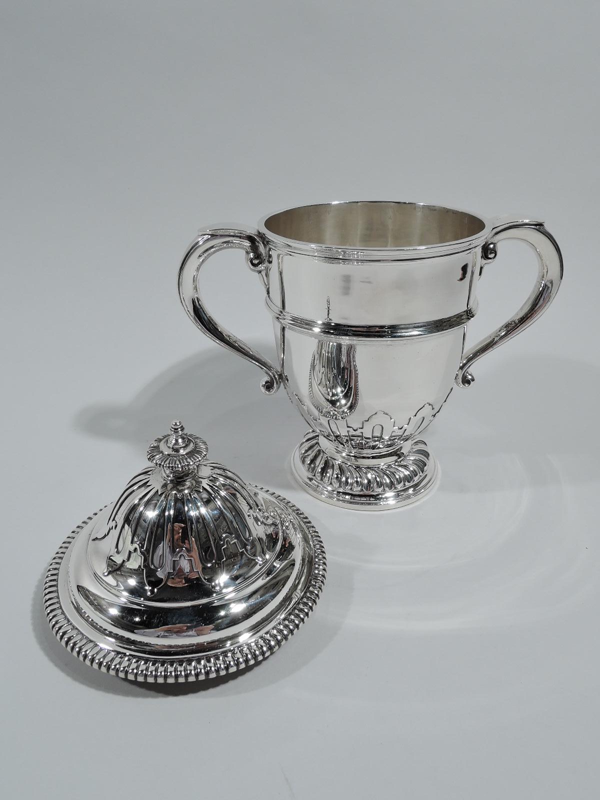 George V sterling silver covered urn. Made by Charles & Richard Comyns in London in 1925. Girdled urn with capped scroll side handles on raised foot. Cover domed. Applied strapwork. Gadrooning and twisted fluting. Traditional Georgian Classical form