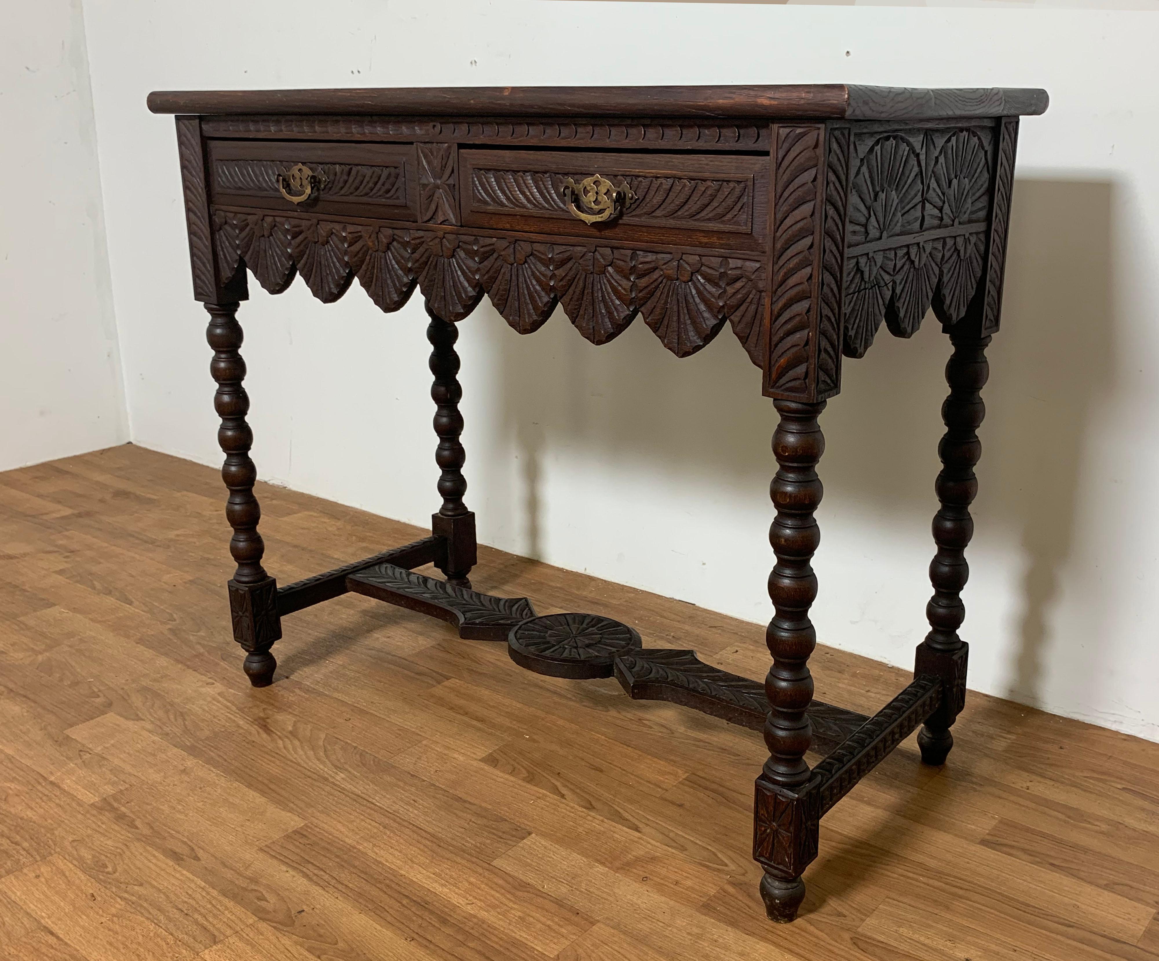 A finely detailed Gothic Revival console table in oak with two drawers, scalloped apron and bobbin turned legs joined by a chip carved stretcher. Extensive carving to the case, drawers and top. Circa 1860s-1880s.