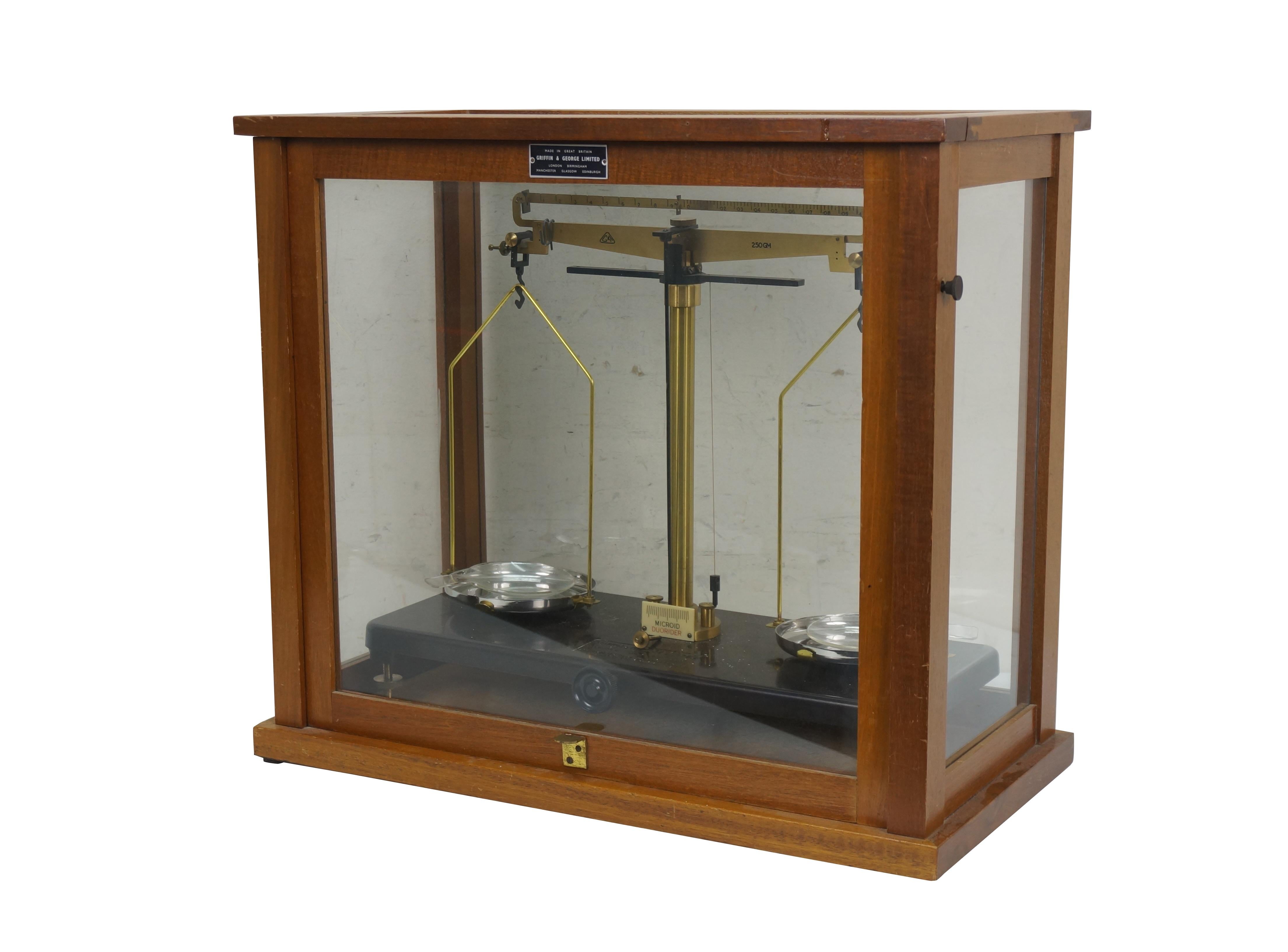 Early 20th-century laboratory / pharmaceutical scales /balances produced by Griffin & George Ltd. of England. Brass and metal scales on a brown bakelite base, housed in a wood and glass case. Plumb bob intact. Includes two Lucite dishes (made in