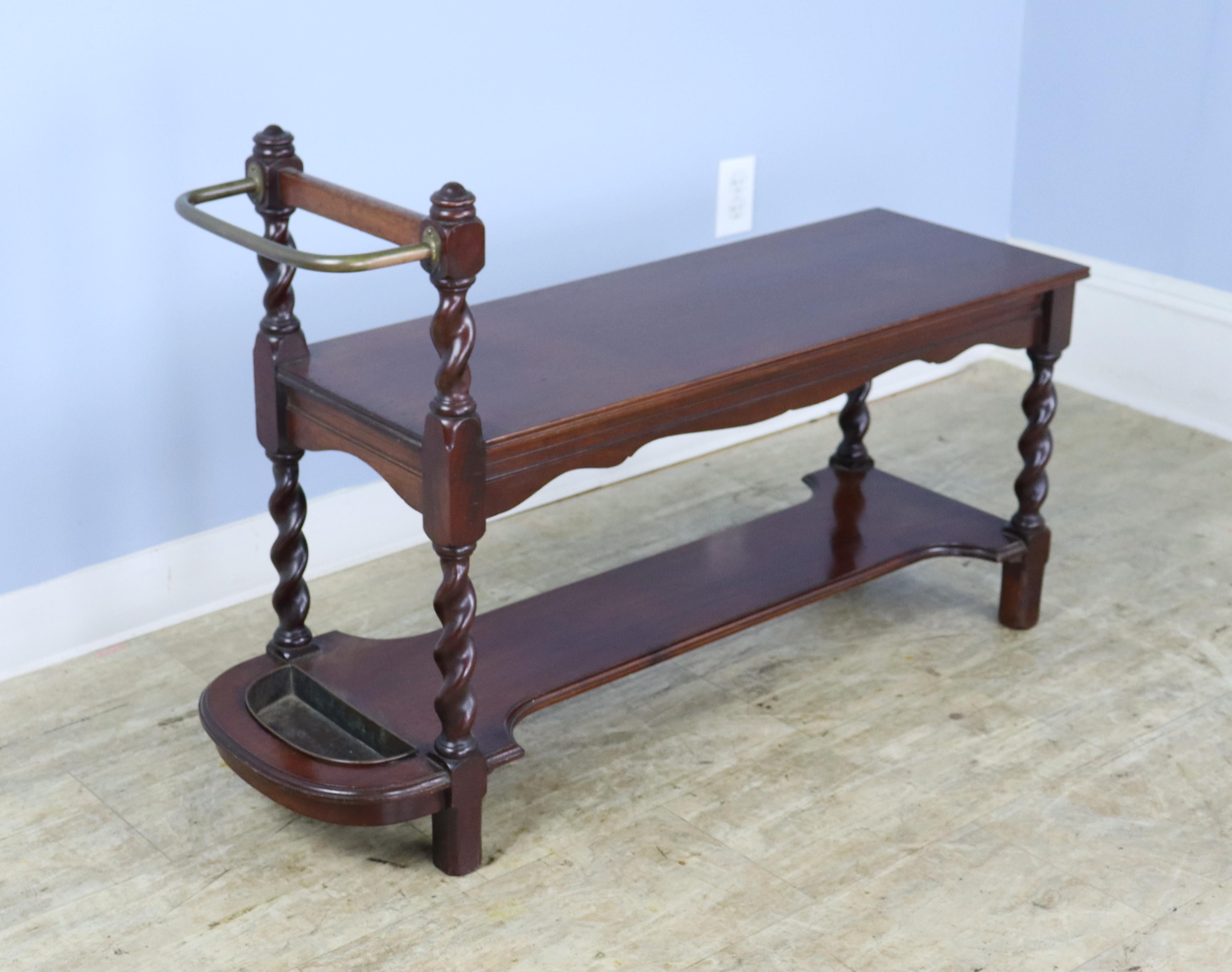 A hall bench in glossy mahogany wih barley twist legs that also serves as an umbrella stand.  