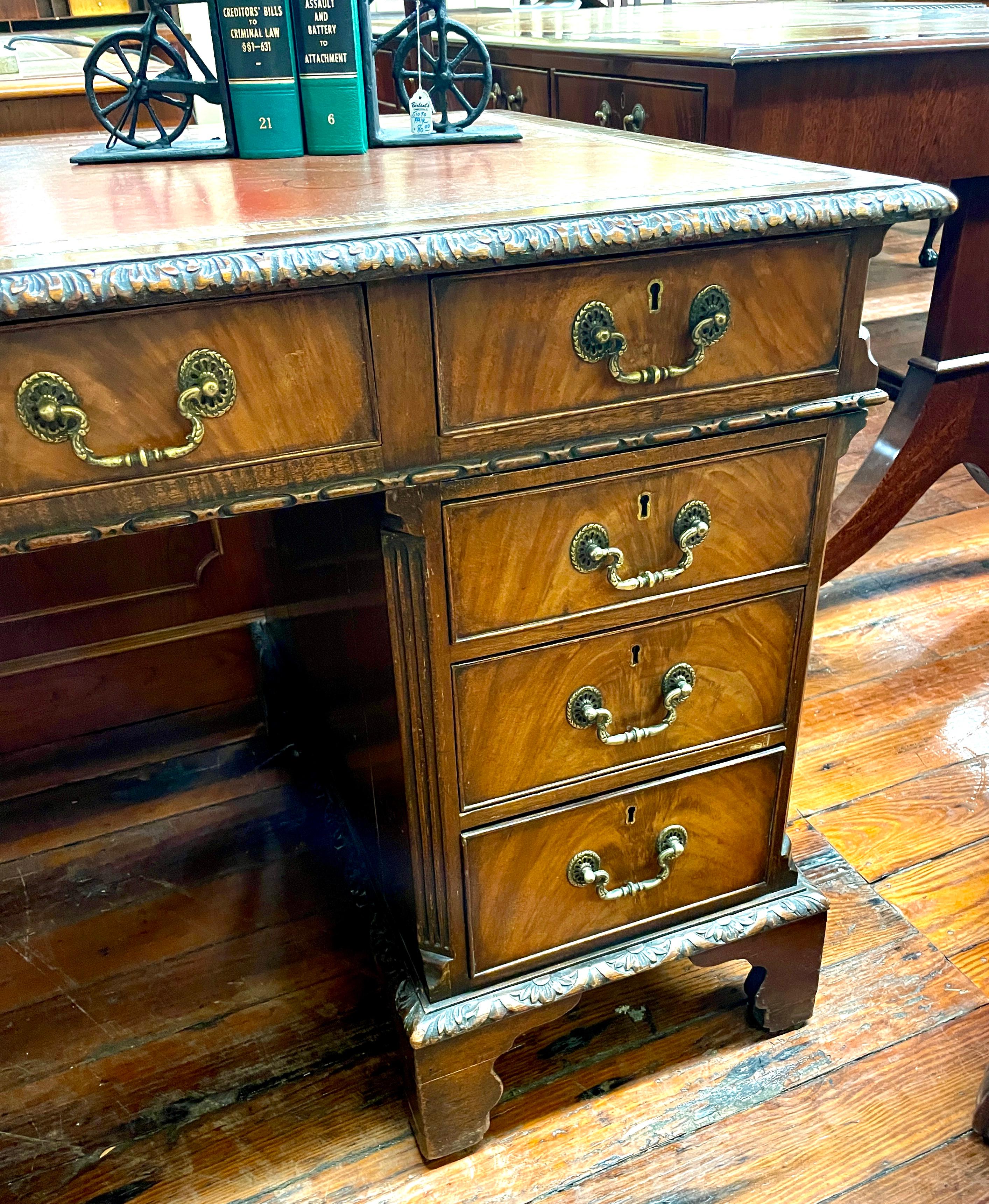 A particularly fine Antique English hand carved mahogany and leather top diminutive Chippendale style pedestal desk with handsome gilt and tooled red-orange leather hide writing surface.  This desk has more than ample kneehole clearance for today's