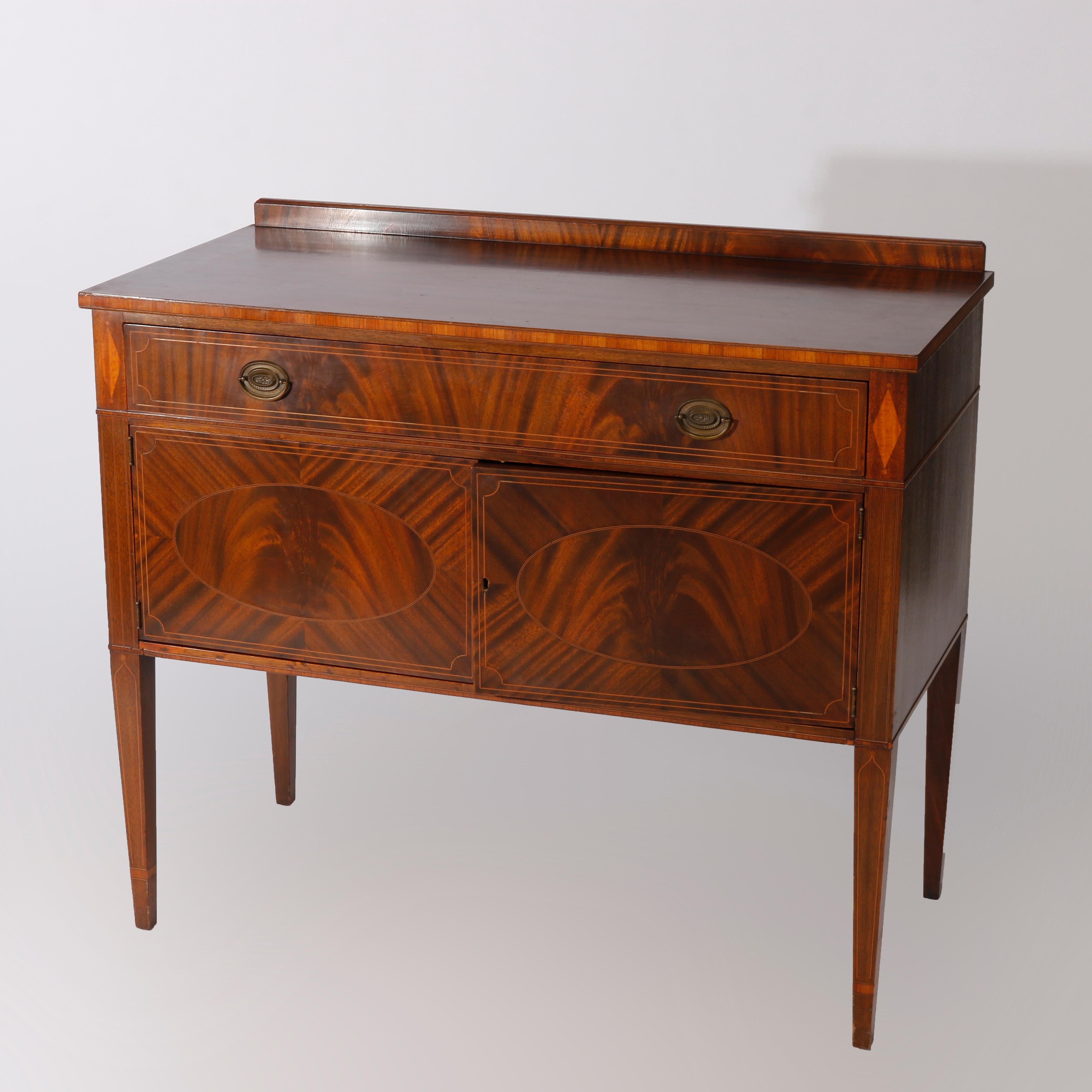 An antique English Hepplewhite style server offers flame mahogany construction with top having shallow backsplash over case with frieze drawer and double door lower cabinet, bookmatched facing and satinwood banding throughout, raised on straight and