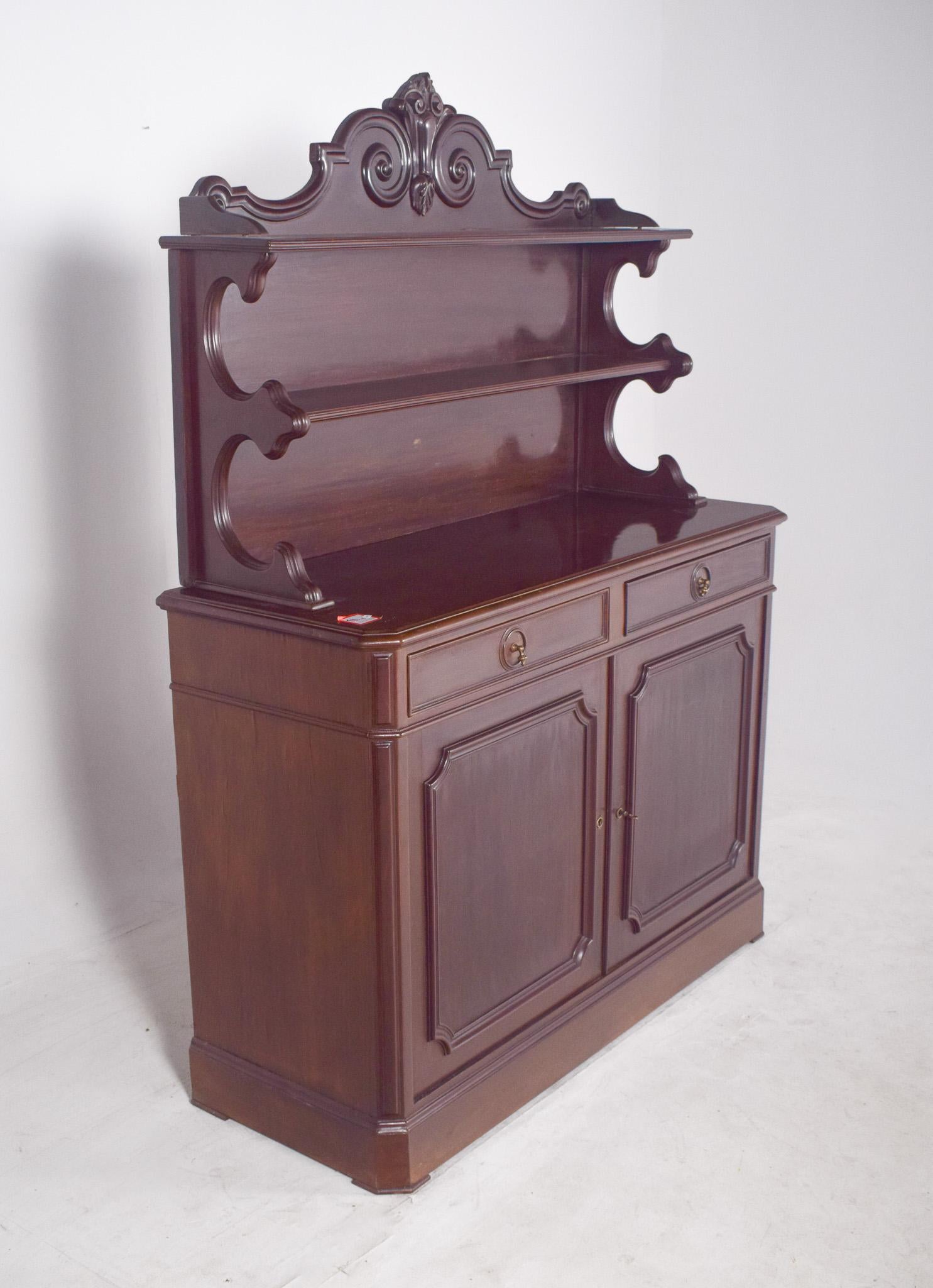 Tall sideboard. In dark wood, it has an imposing and classic presence, with features that evoke Victorian-inspired furniture. Its robust body is divided into two distinct parts, the lower one with two carved doors and two upper drawers, and the top
