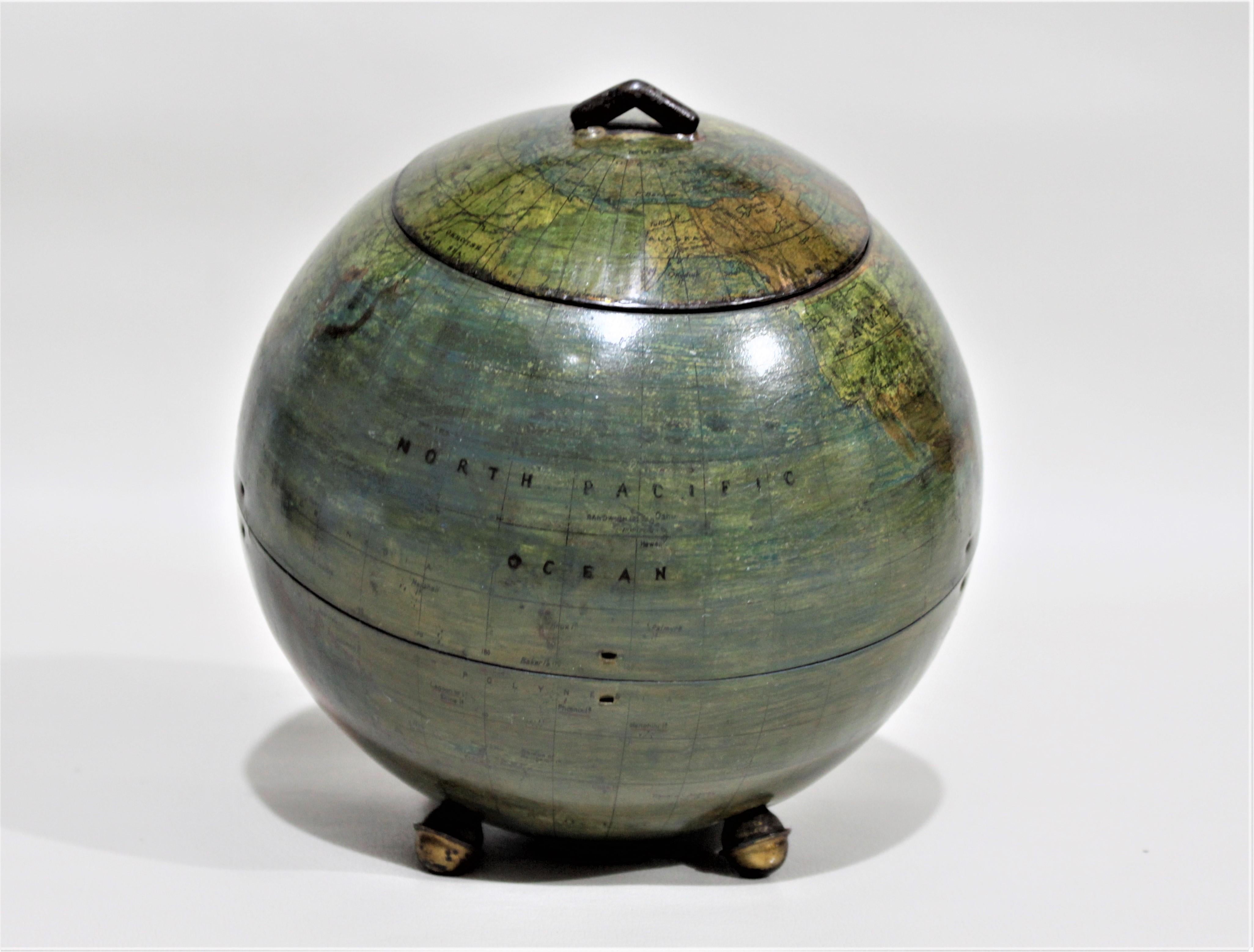 This antique figural biscuit tin dates to circa 1910 and was produced by Huntley & Palmers of England. The tin is fashioned as a world globe and sits on four bun feet. The tin is tilted back slightly and has a hinged lid with a small handle at the
