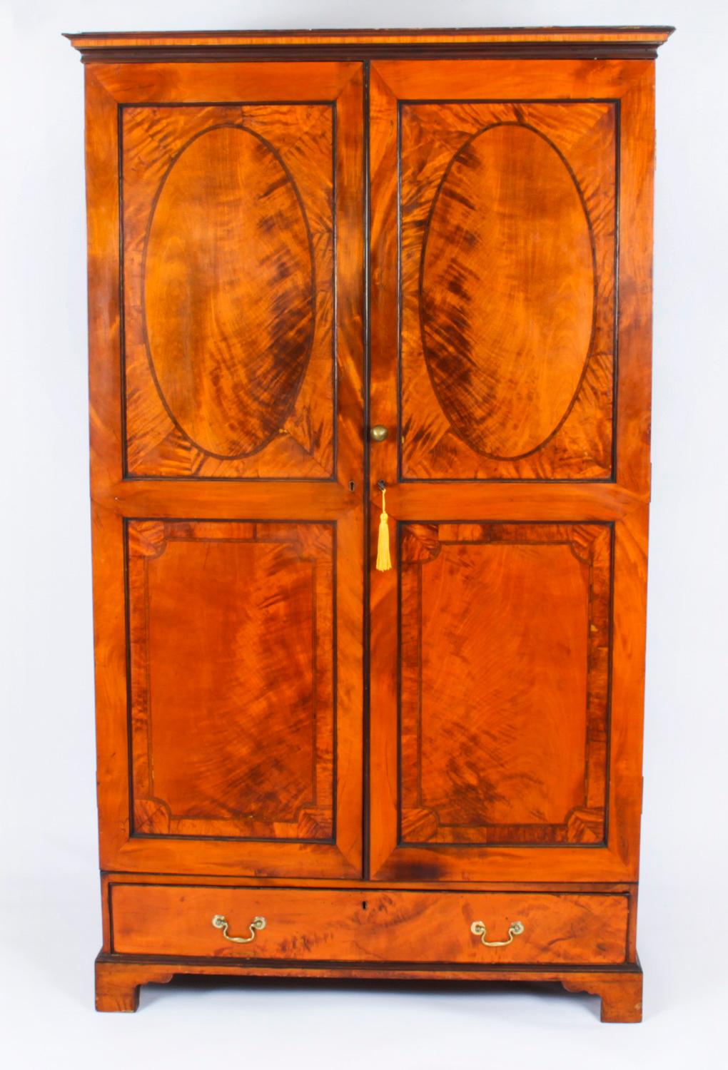 This is an impressive antique English Victorian Sheraton Revival satinwood wardrobe, circa 1850 in date.

The pair of doors each with oval and rectangular flame satinwood panels with decorative ebonised stringing and crossbanding.

The doors