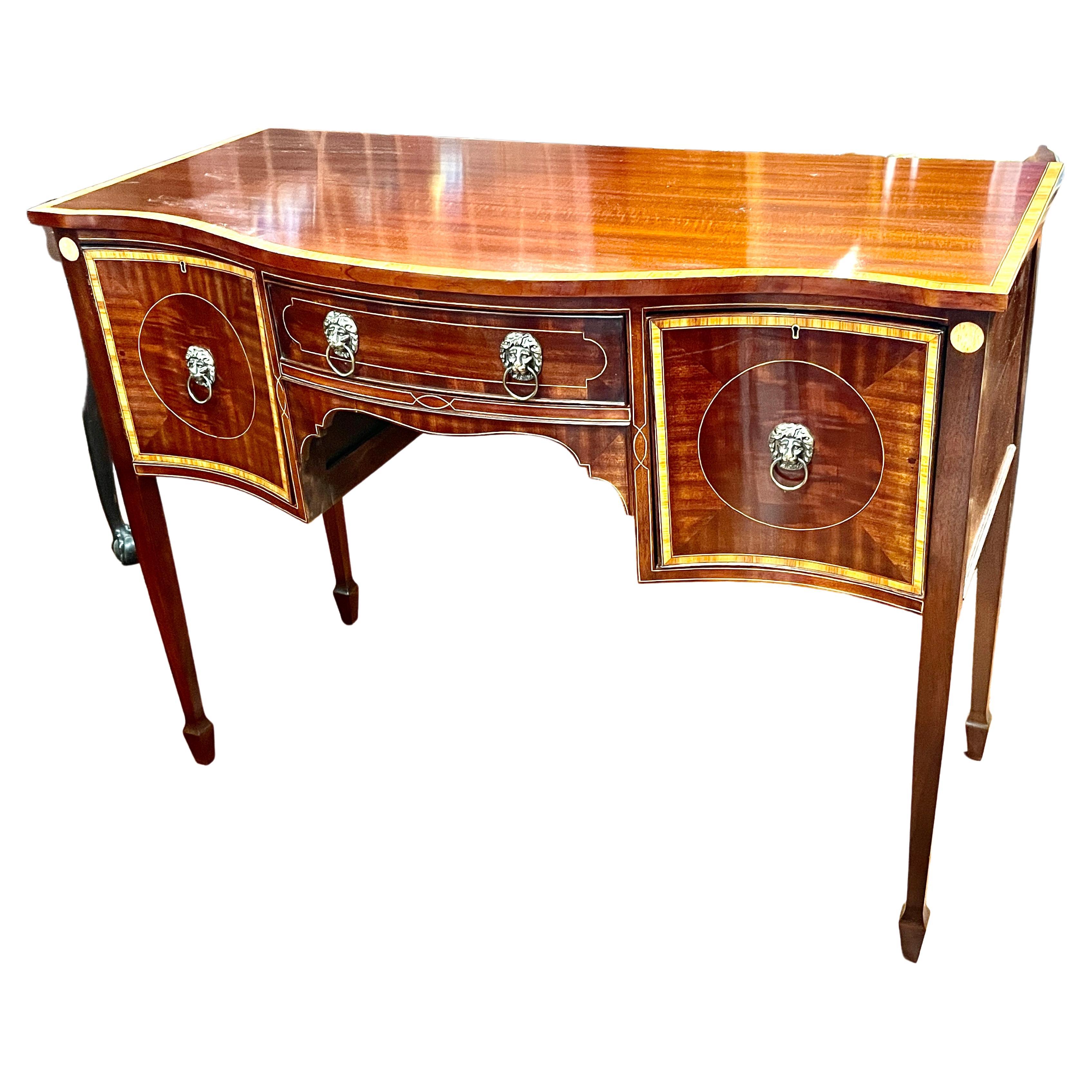 Gorgeous antique English inlaid mahogany Hepplewhite style serpentine sideboard with tulipwood cross-banding and handsome Regency style cast brass lion's head pulls. Cellarette drawer on right side and cupboard on left. Extraordinary tulipwood