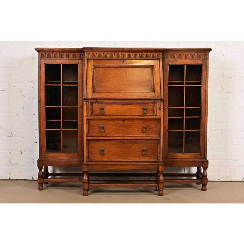 Extraordinario mueble librería doble jacobeo inglés con cajonera y escritorio con frente abatible

A la manera de Berkey y Gay

Inglaterra, hacia 1920

De roble tallado, con puertas delanteras de cristal ajimezadas y herrajes originales de latón.