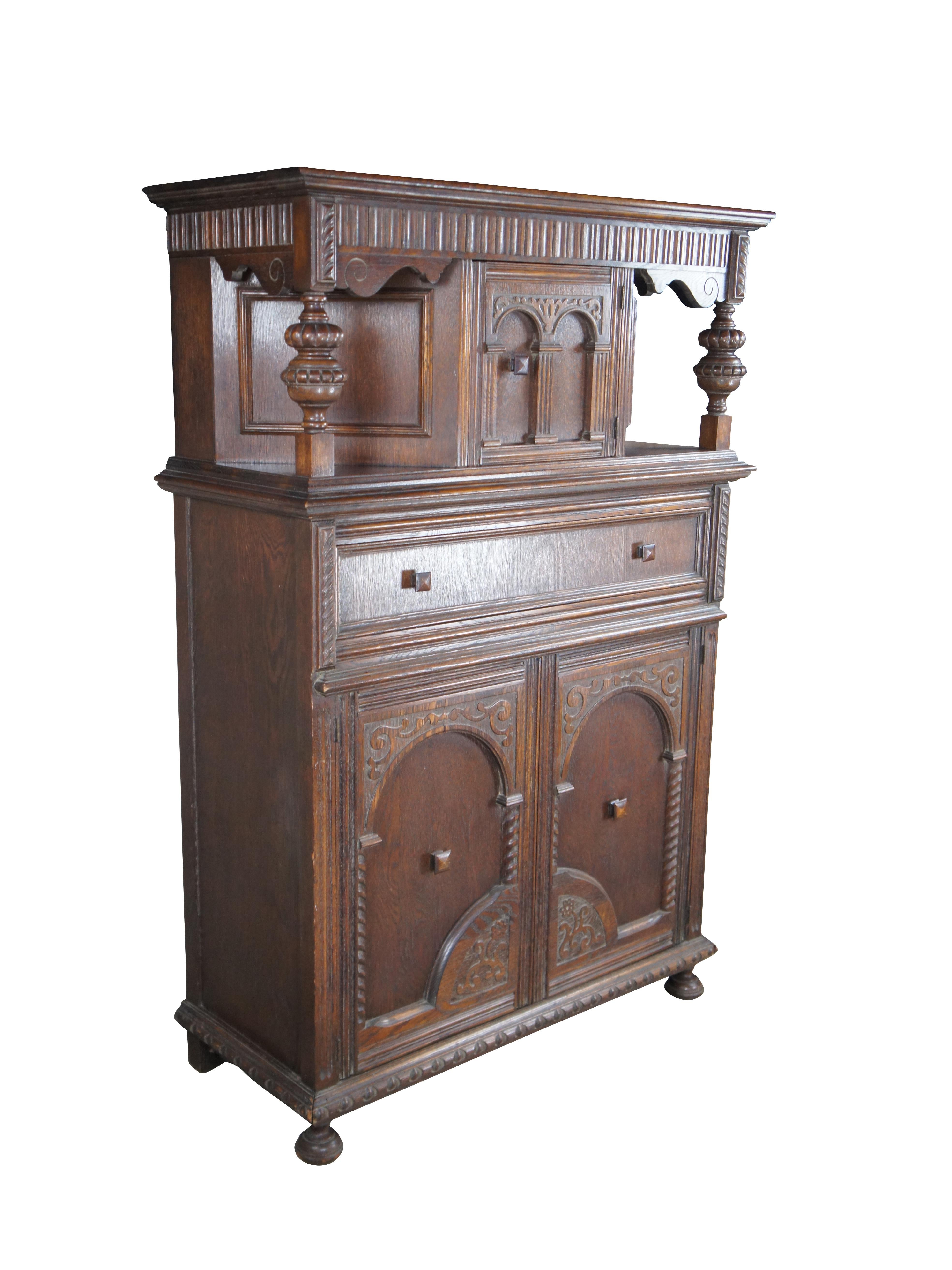 An exceptional Jacobean style Court Cupboard, Circa 1920s. Features a tall case with upper hutch between robust turned baluster supports and scrolled spandrels. Upper apron has fluted paneling in a linen fold manner. Below is a large central