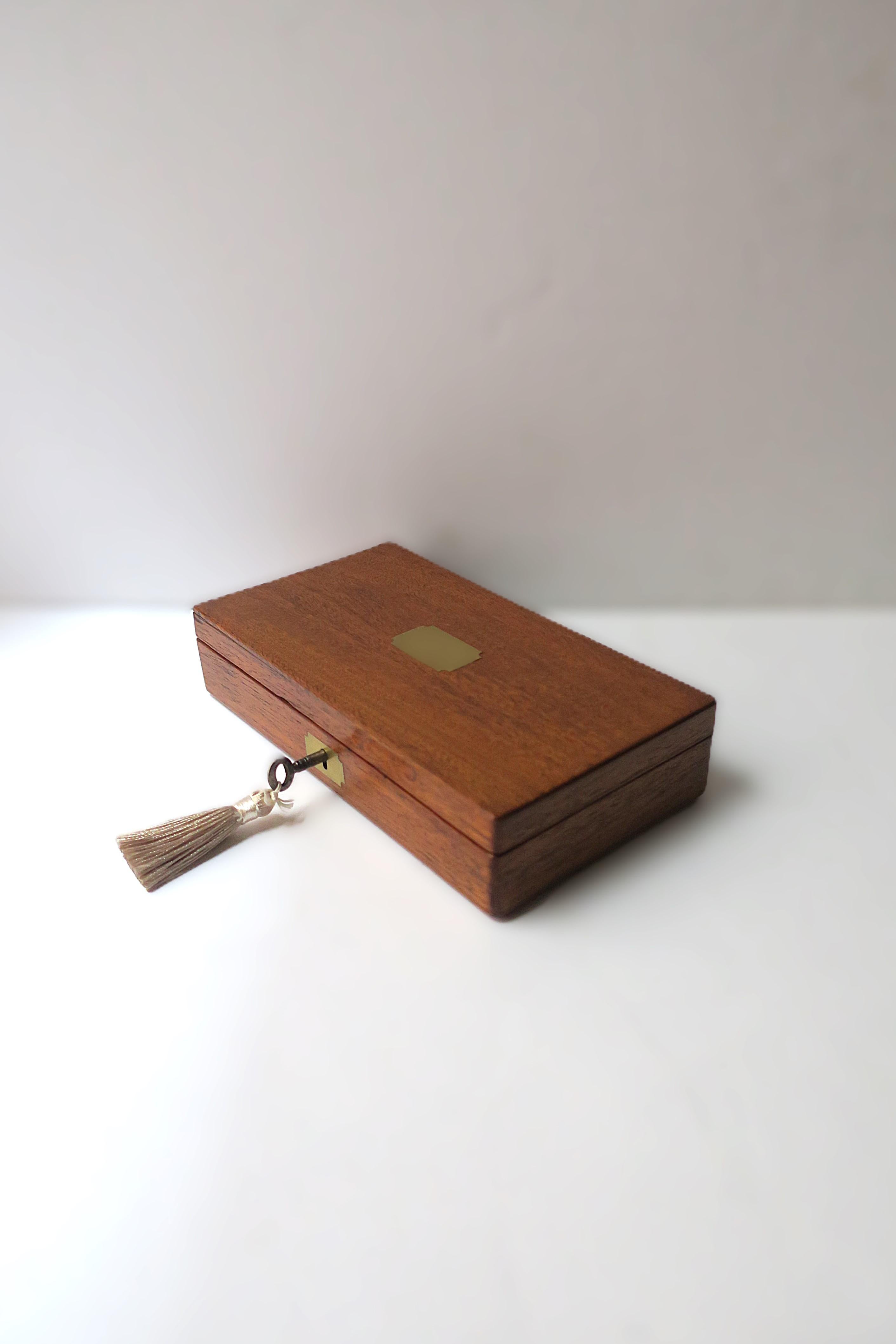 A beautiful antique English wood jewelry box with tray and key, circa early-20th century, England. Box is rectangular, wood, coordinating brass accent on top lid and at front lock, velvet lined, removeable tray, finished with a steel key with silk