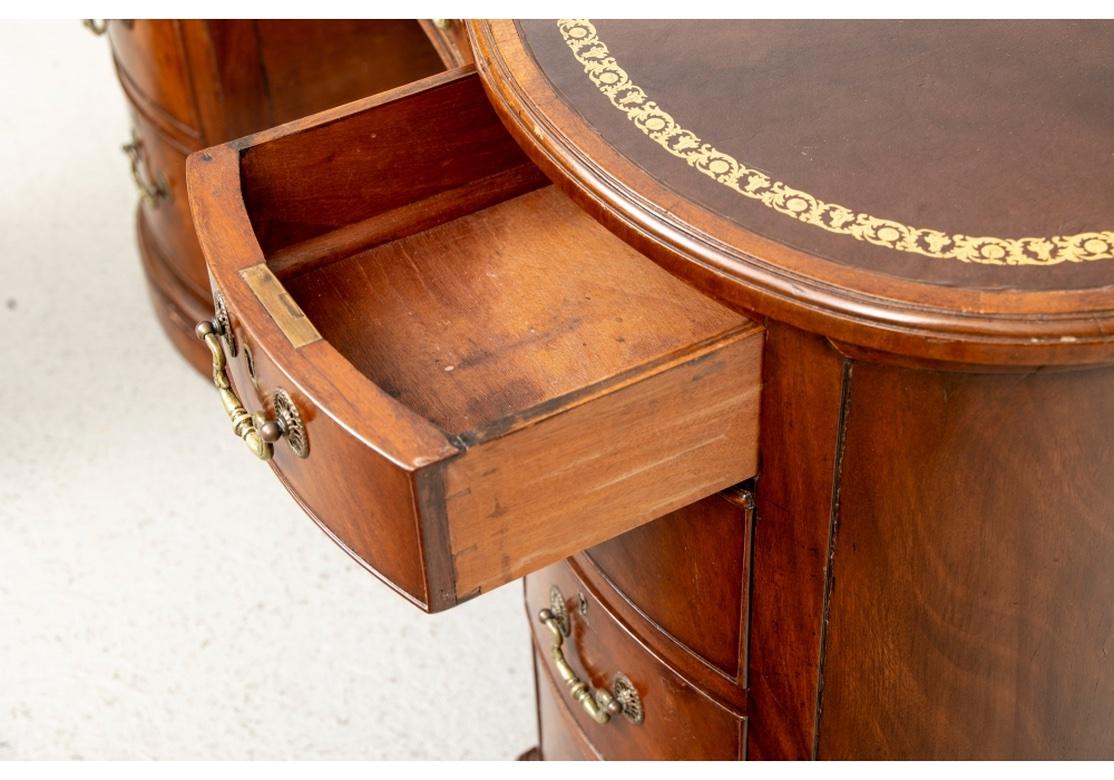 Mahogany kidney form desk with gilt-embossed brown leather top (The Leather top replaced at a later time). The desk with a center drawer flanked by 4 drawers each side on front. Finished on both sides and resting on a plinth base. Lacking a