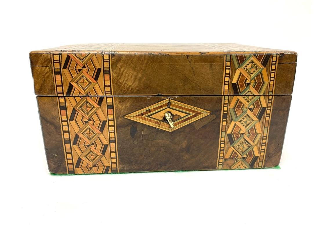Antigua caja inglesa Tunbridge con incrustaciones geométricas, tapa abatible, interior de terciopelo rojo, fondo de fieltro y viene con llave que funciona. Caja con medallón incrustado en forma de rombo flanqueado por bandas de formas geométricas de