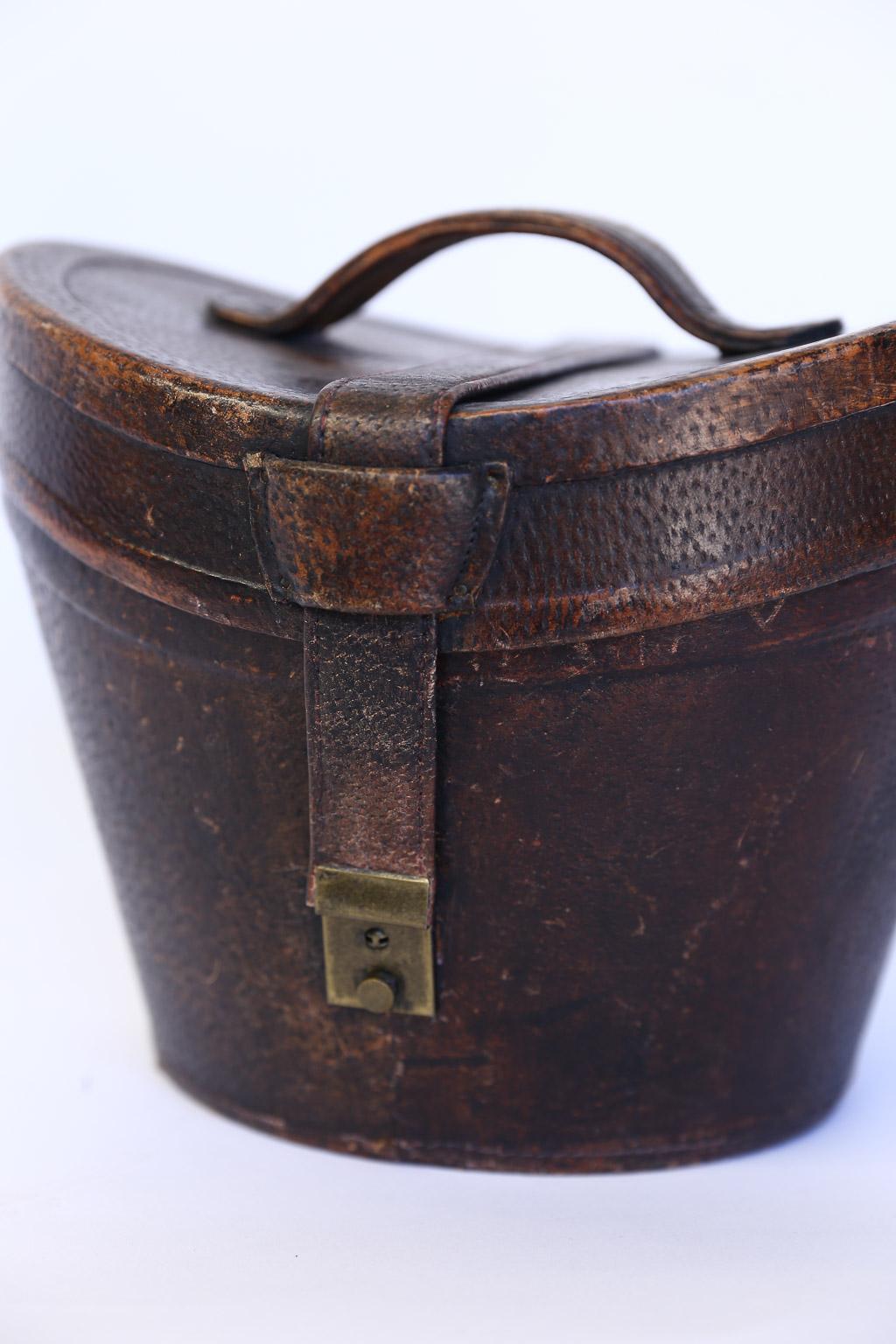 This is a beautiful English leather hat box. It was once used to store a top hat. The box is in good condition with a front brass lock and leather carrying handle on the top. The box is lined with velvet and ready to store your hat or display in
