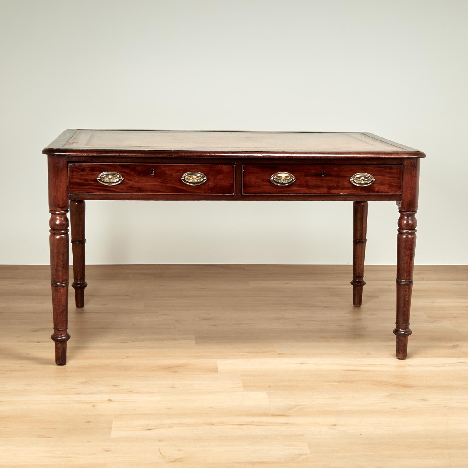 Handsome 19th century English desk handcrafted in mahogany with the original tooled leather top on a case with two drawers and brass hardware set on classic turned legs. 