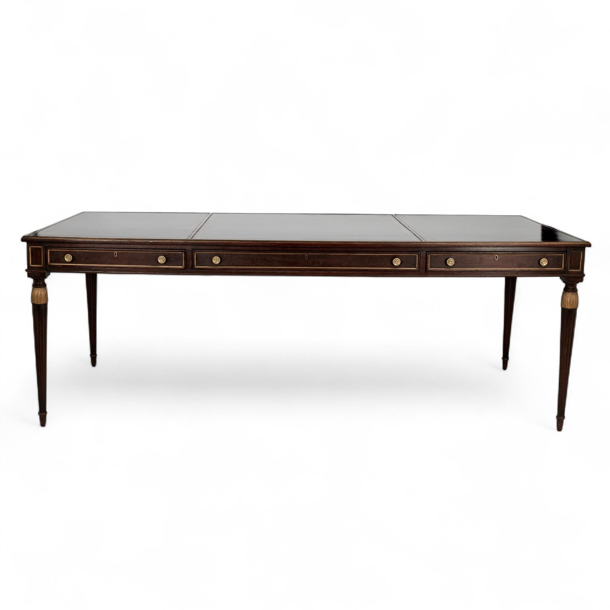 Long et élégant bureau anglais ancien de style néoclassique avec trois panneaux en cuir estampé sur le dessus d'un boîtier comportant trois tiroirs avec quincaillerie en laiton sur quatre pieds fuselés et cannelés avec des glands sculptés et dorés. 