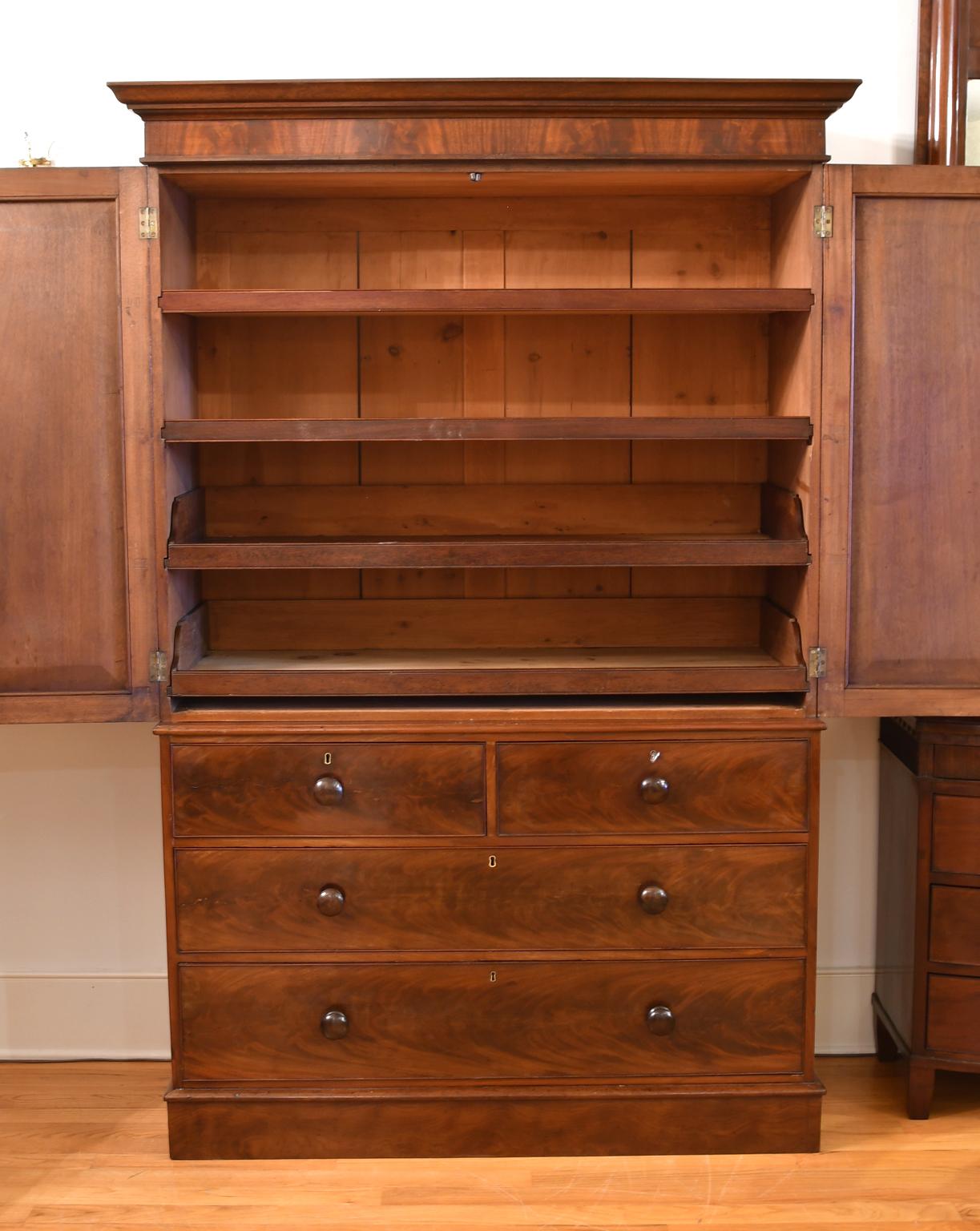 An English Regency linen press in fine West Indies mahogany with two cabinet doors over base containing two drawers over two longer storage drawers. Interior offers 2 sliding shelves & 2 sliding trays. Features a handsome figuring of the wood grain