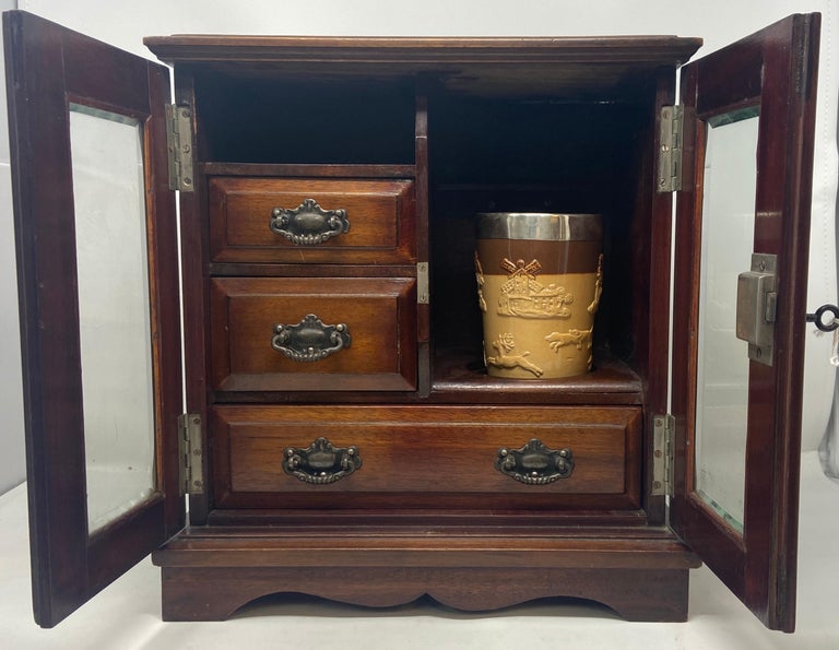 Antique English Victorian Mahogany and Beveled Glass Gentleman's Smoking box with interior drawers and Royal Doulton porcelain tobacco holder/mixer, Circa 1890-1910.
Please note that the bottom drawer has a central slat that can be moved or removed