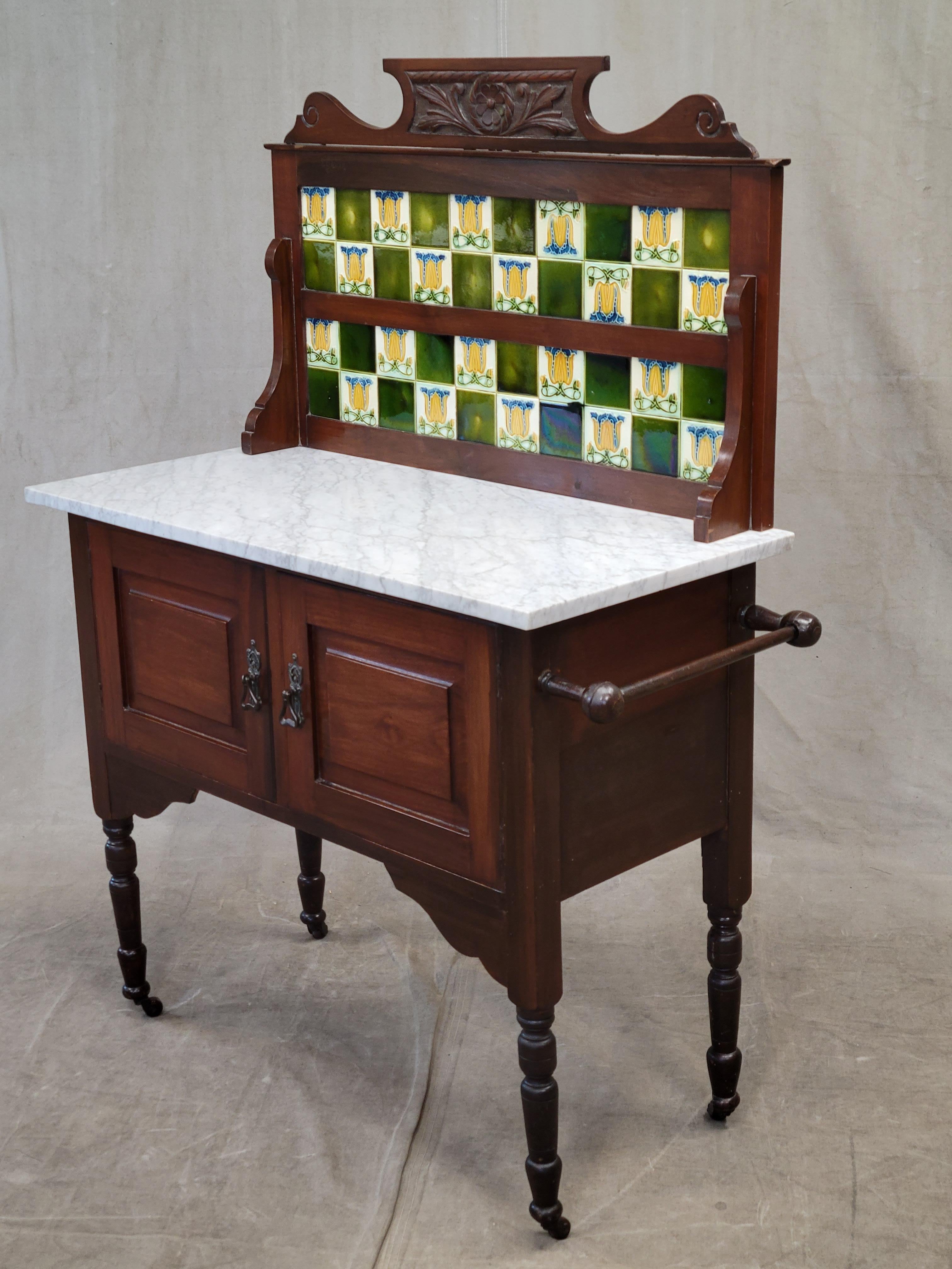 Such a charming antique English mahogany washstand with Carrara marble top and green tulip tile backsplash. In original but very good condition. The towel bar, marble and tile are all original to this piece. The wood bears the original finish and