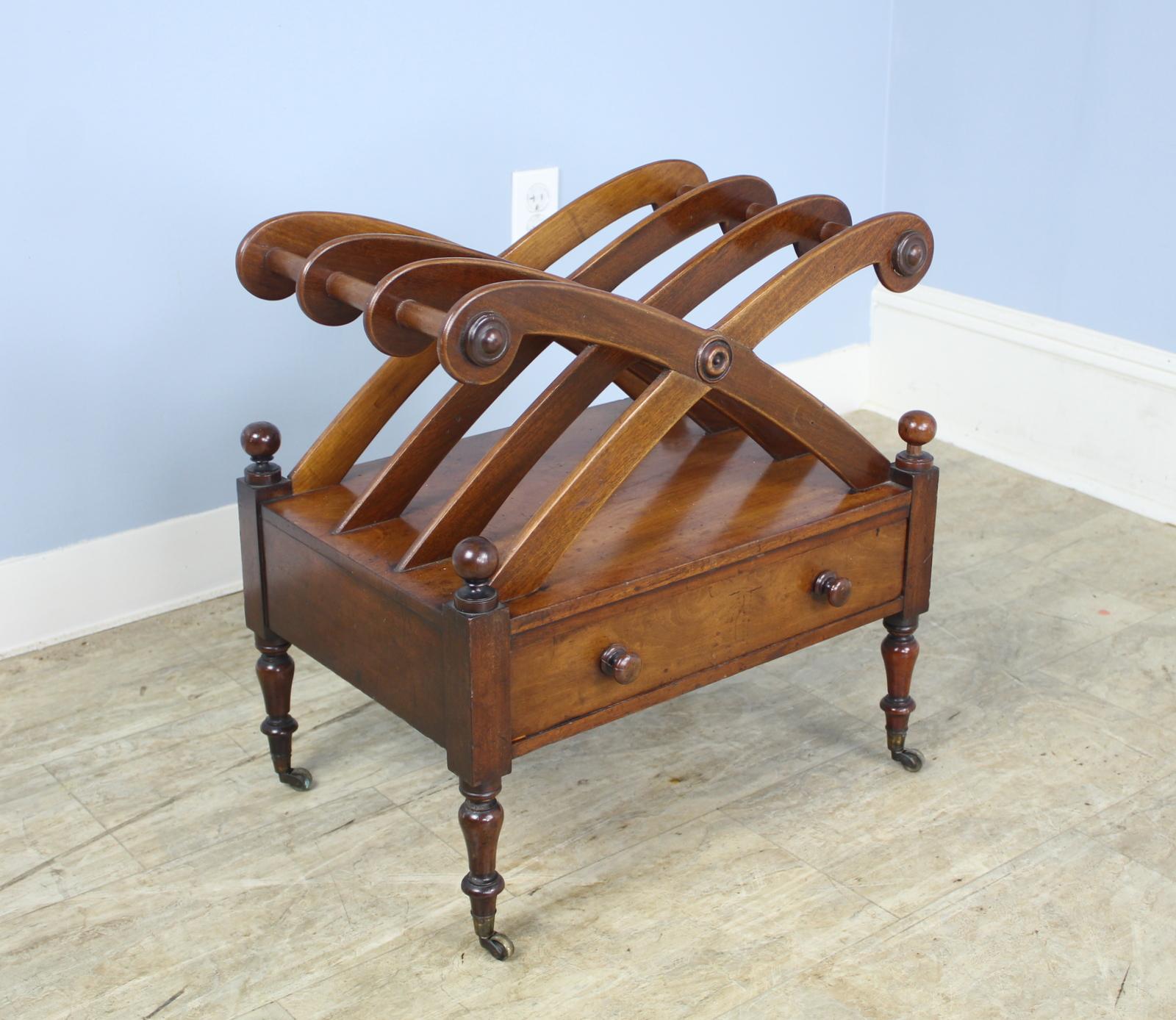 A handsome mahogany canterbury or magazine rack, originally used to organize sheet music. Stylized carved rack with a single drawer in front and shaped legs standing on brass castors.