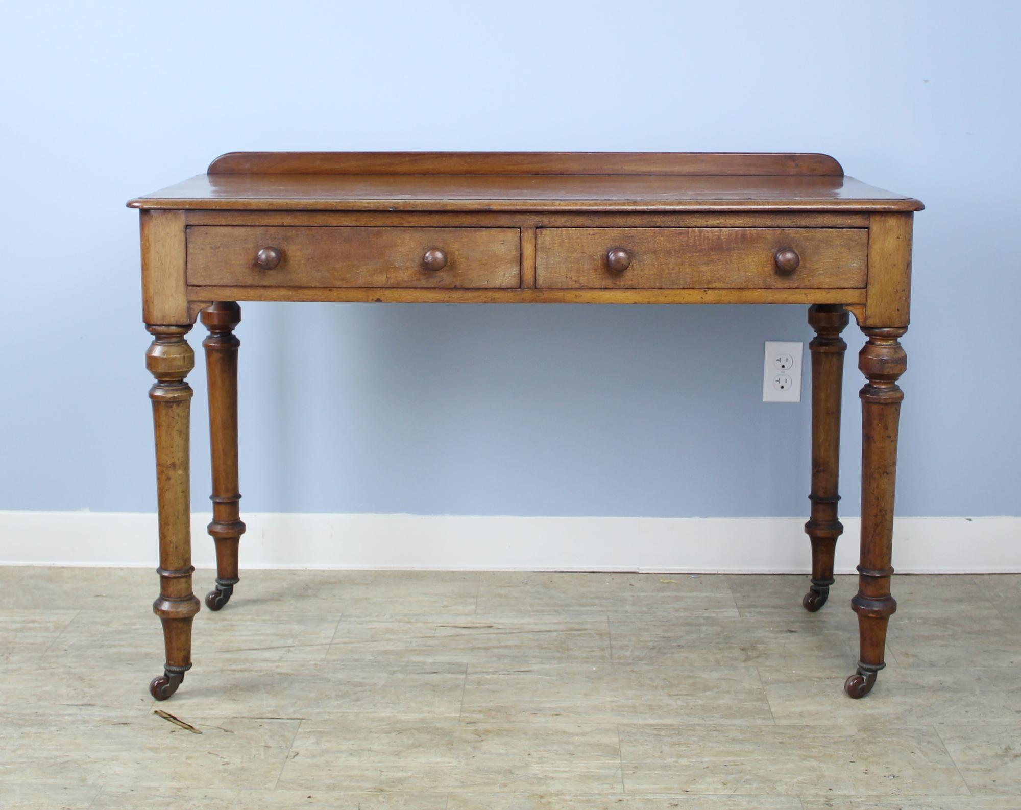 A handsome small desk with classic turned legs on original castors. Nice mellow color and good patina. Two roomy drawers and an apron height of 25 inches good for knees. Galleried back adds period charm. Note: the two knobs on the right drawer are