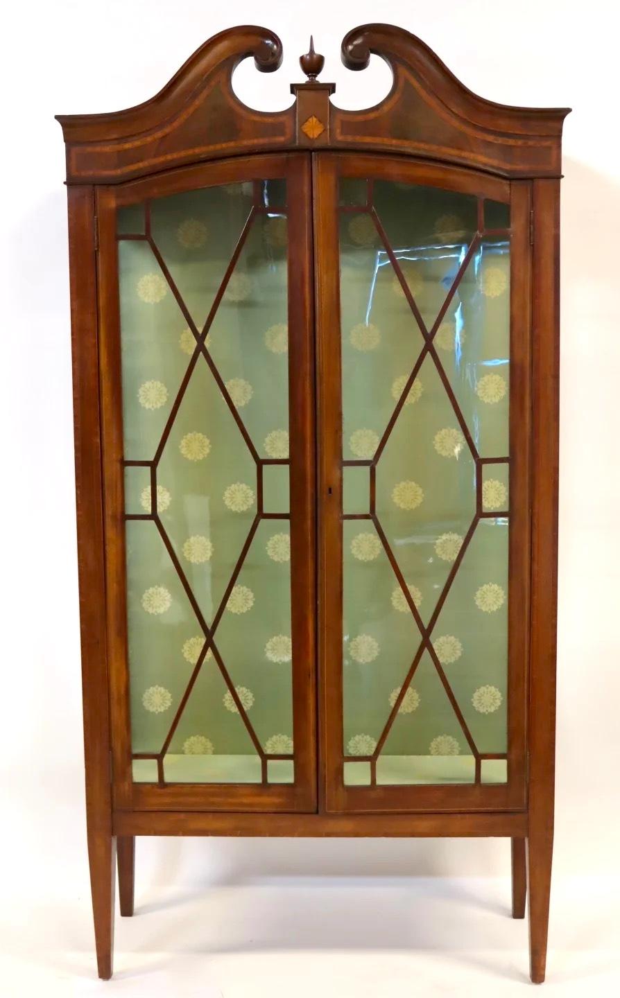 Refinada vitrina inglesa de caoba, fechada en el segundo cuarto del siglo XIX y ejecutada en estilo eduardiano. Esta elegante vitrina está finamente elaborada con una corona de caoba tallada coronada por un remate central, sobre dos puertas de