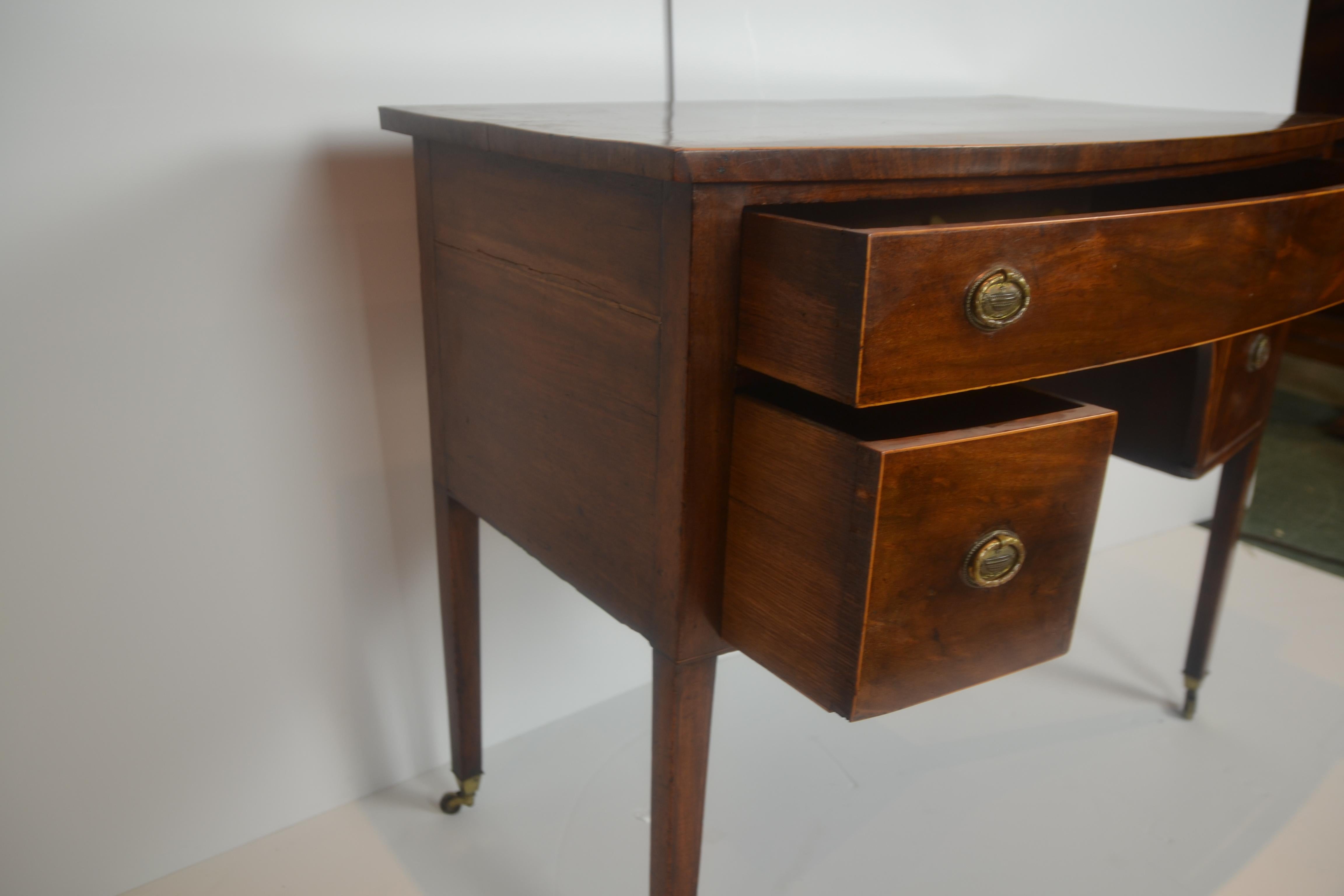 A charming small size English lowboy in old wide-grain mahogany. Drawers are oak lined and fitted with oval brass pulls decorated with an urn. Lower legs and top edge are string inlaid. Feet have brass toe-caps and castors. c.1790.