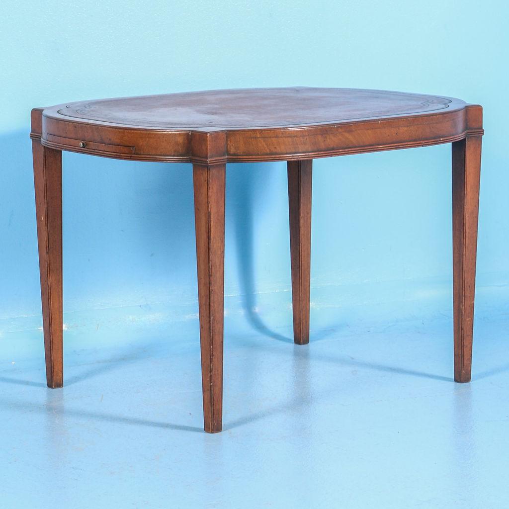 This charming English mahogany side table from the mid-20th century features the original embossed leather inlay on top, along with opposing pull out sides on either end. With tapered legs, this elegant yet simple table would look wonderful in any