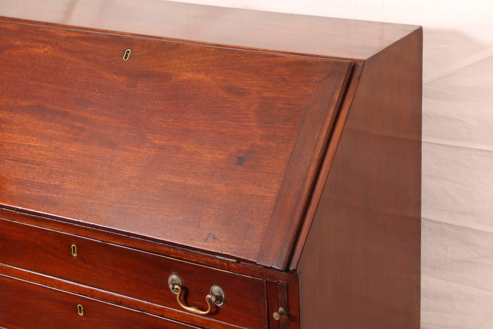 Antique George III English slant front desk, mahogany, four graduated drawers with brass keyholes and handles, slant front with pull out supports an a brass keyhole, opening to cubby holes and drawers, whole raised on bracket feet, lacking keys.