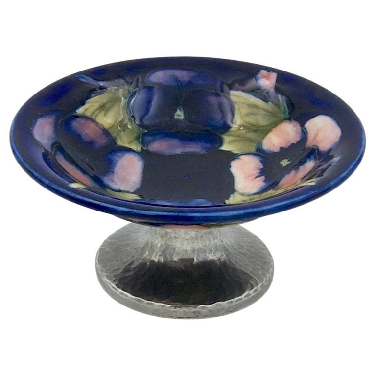 A circular Moorcroft tazza dish on an outswept Tudric pewter pedestal base, made in England for Liberty & Co. of London and dating circa 1920. The art pottery dish or shallow bowl was designed by William Moorcroft (British, 1872–1945) and skillfully