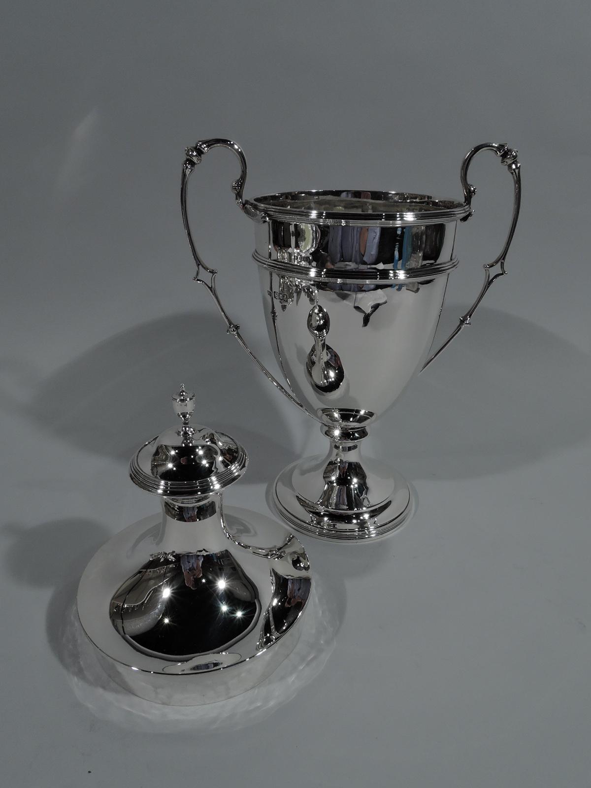 George V sterling silver trophy cup. Made by Lionel Alfred Crichton in London in 1916. Traditional amphora with ovoid body on knop on stepped foot. High-looping leaf-mounted side handles. Domed cover with vase finial. Lots of room for engraving with